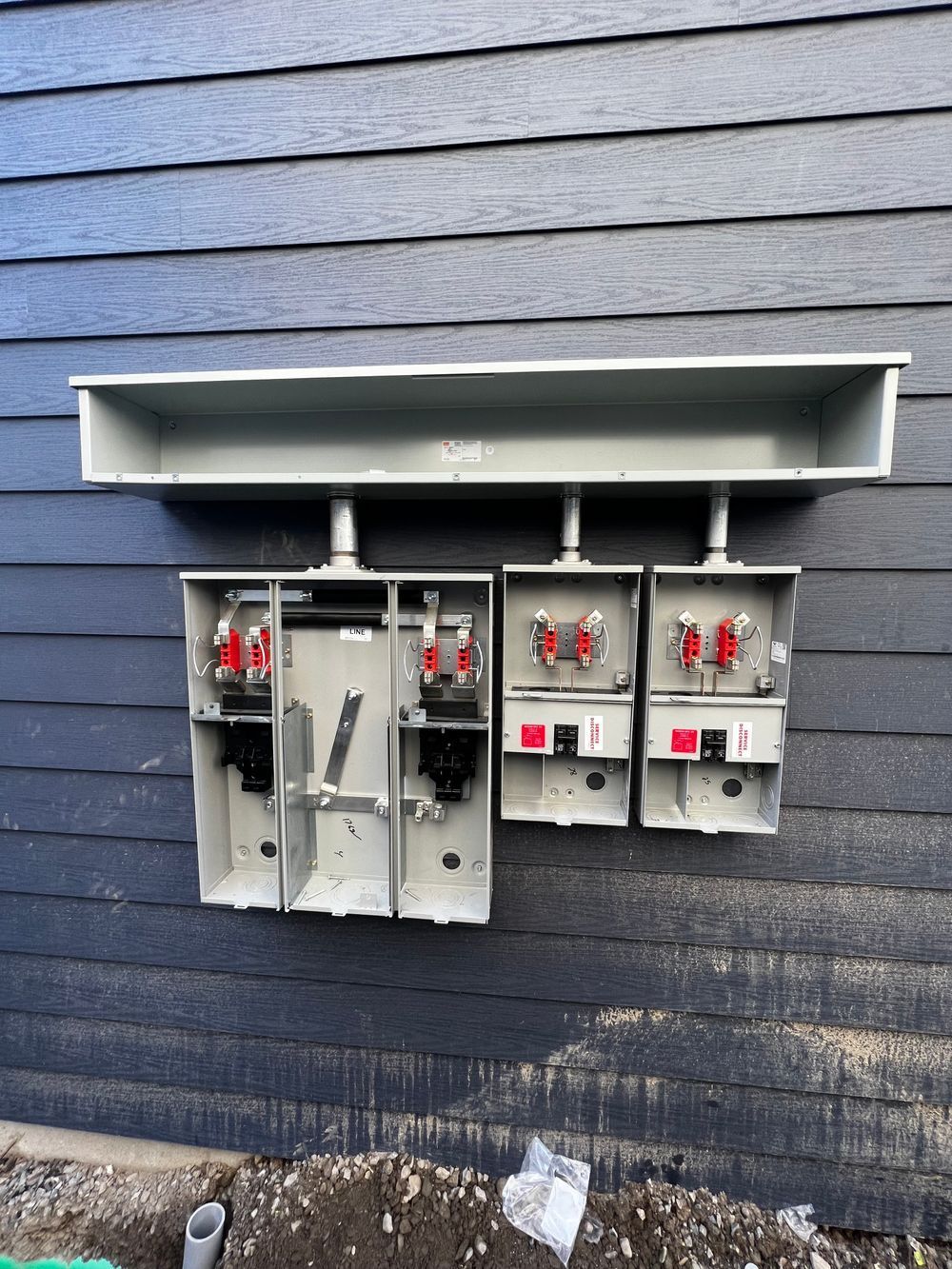 Three electrical boxes are hanging on the side of a building