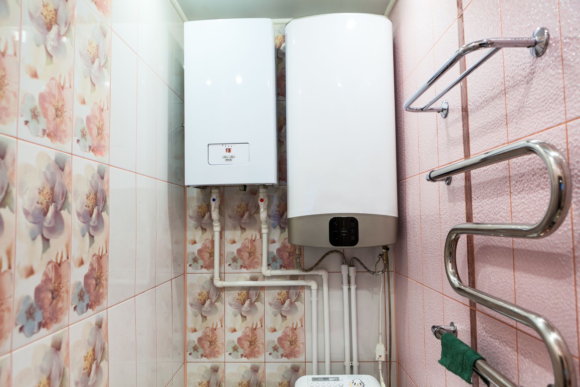 Two white water heaters mounted on a tiled wall in a bathroom, with towel racks.