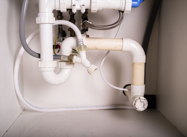 White plumbing pipes under a sink with a curved drain and connected water lines.
