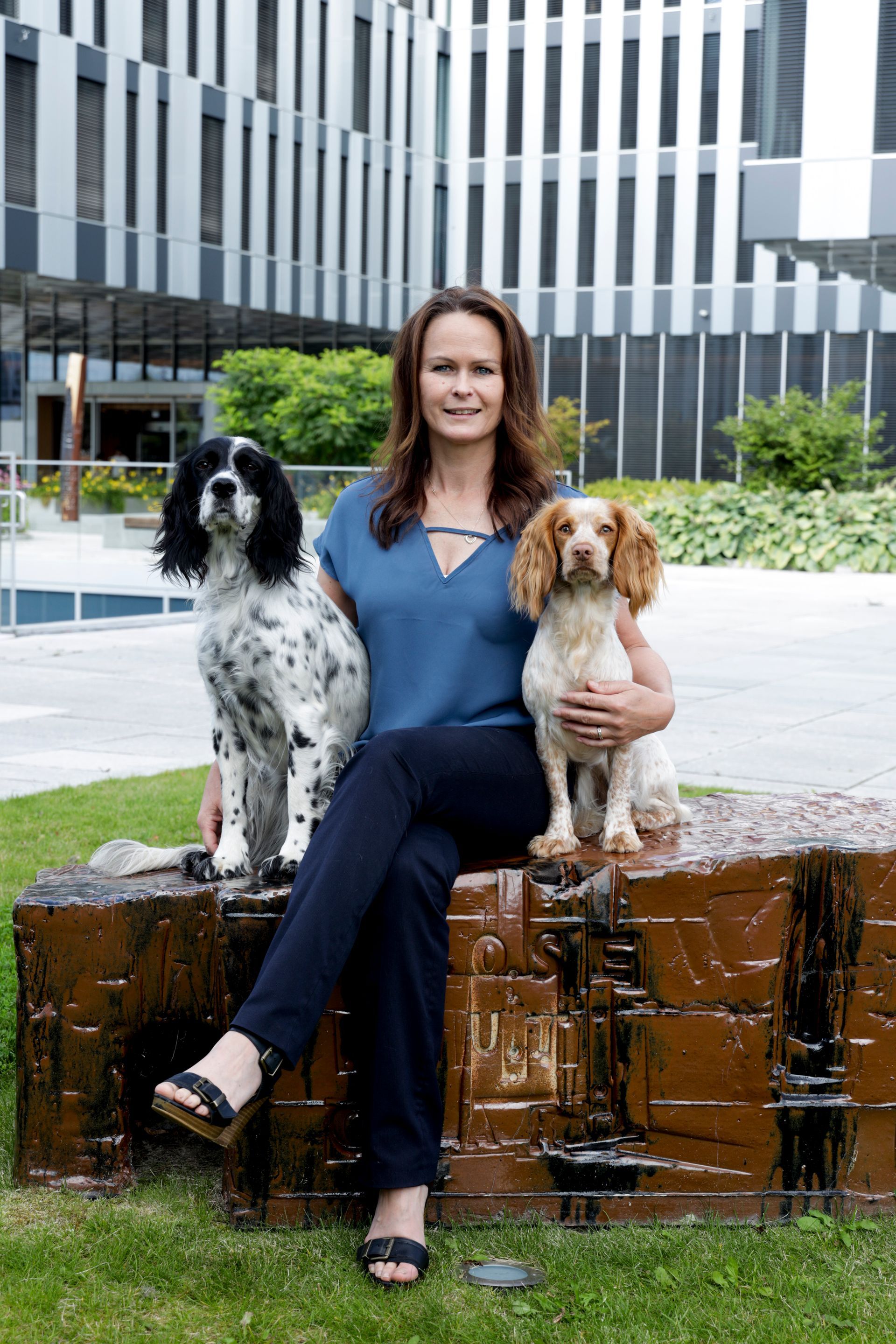 Woman seated with two dogs in front of a building. The dogs are a black and white and a golden color.