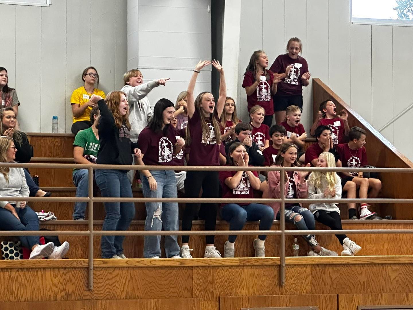 A group of students are sitting on the bleachers cheering on teams at Bible Knowledge Day.