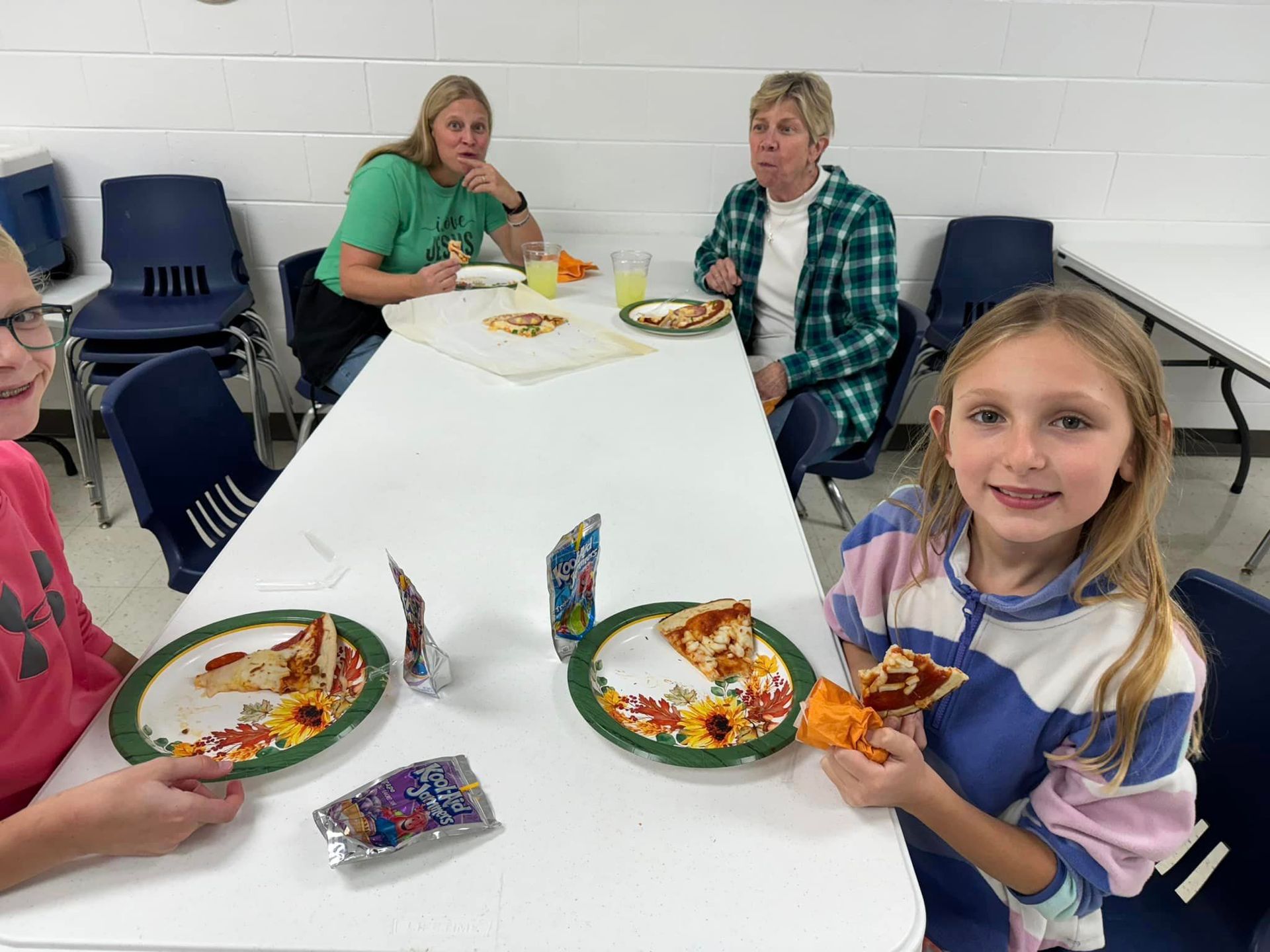 A group of people are sitting at a table eating pizza at a PTL meeting.