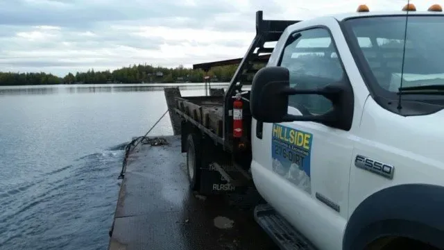 A white hillside tow truck is parked next to a body of water