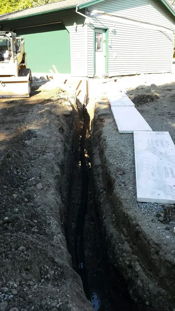A large trench is being dug in front of a house.