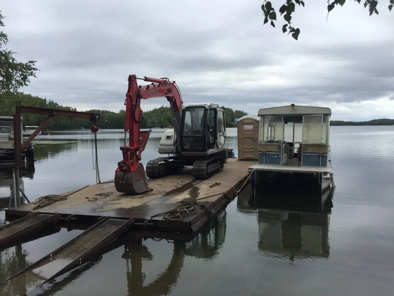 An excavator is sitting on a dock next to a boat.