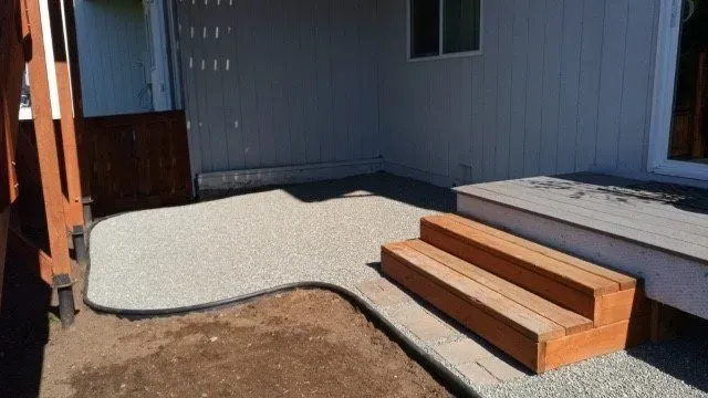 A patio with wooden steps and gravel in front of a house.