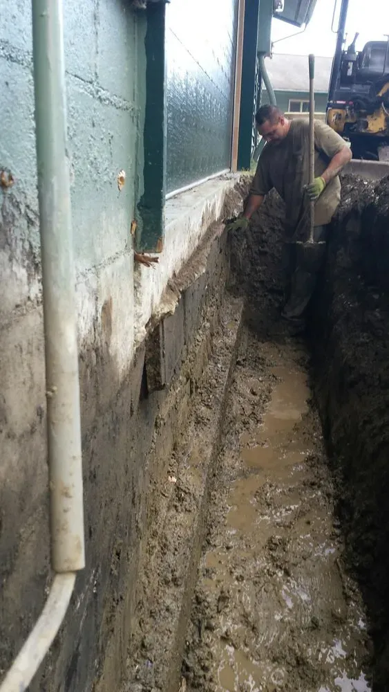 A man is digging a hole in the ground next to a building.