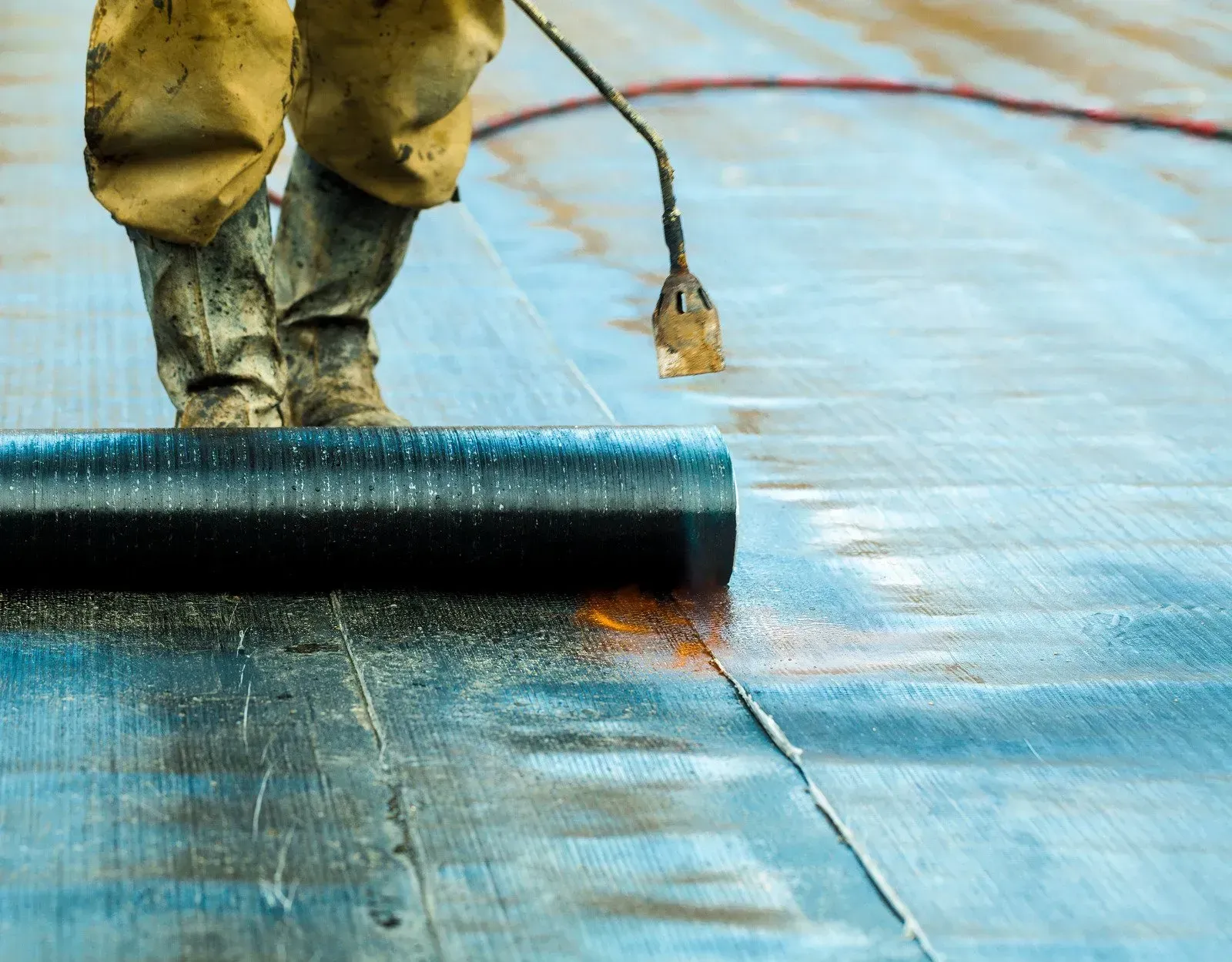 A person is rolling a roll of waterproofing on a roof.
