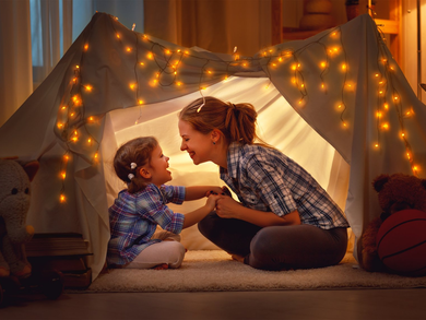 Happy mother and daughter playing at home in tent .