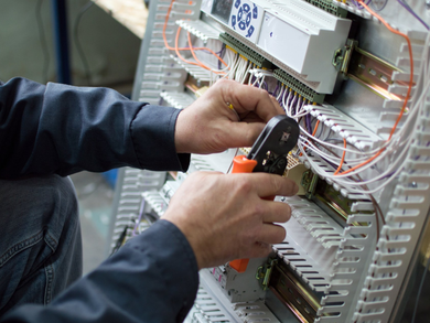 Hands of electrician assembling industrial HVAC control cubicle in workshop