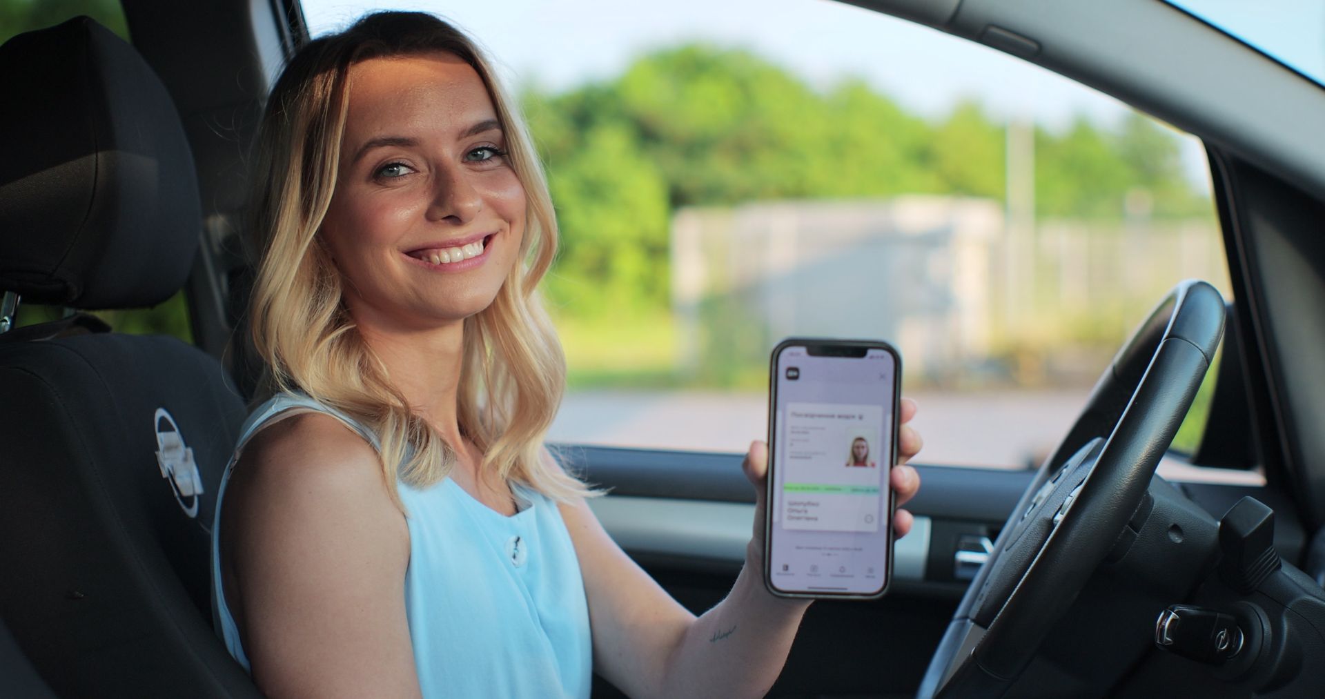 Une femme est assise dans une voiture et tient un téléphone portable.