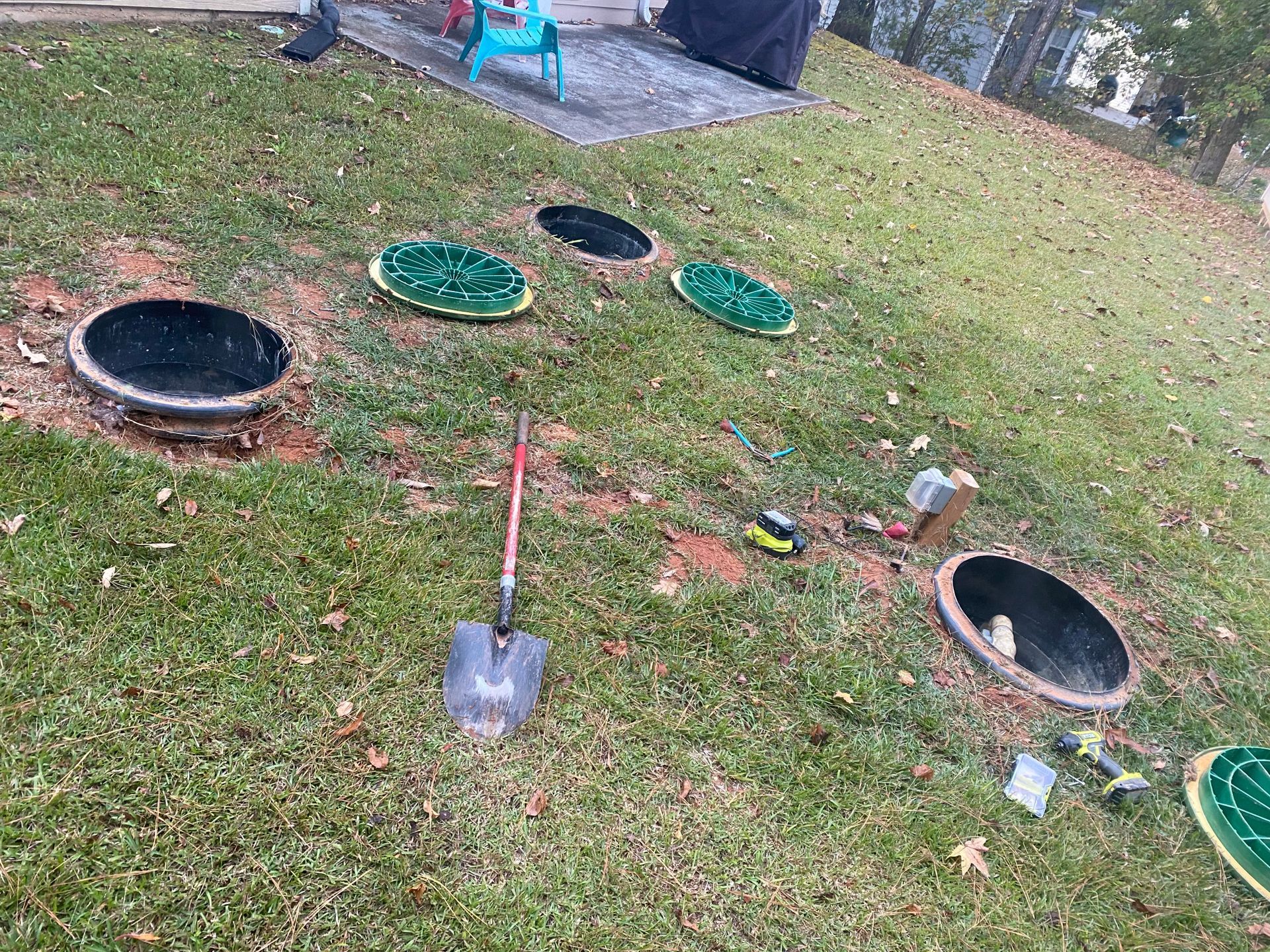 A shovel is sitting in the grass next to a row of septic tanks.