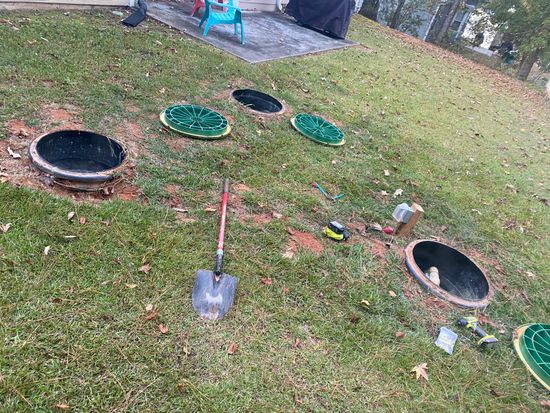 A shovel is sitting in the grass next to a row of septic tanks.