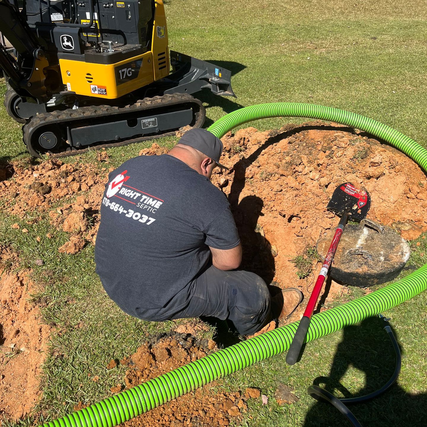 A man is kneeling in the dirt next to a green hose.