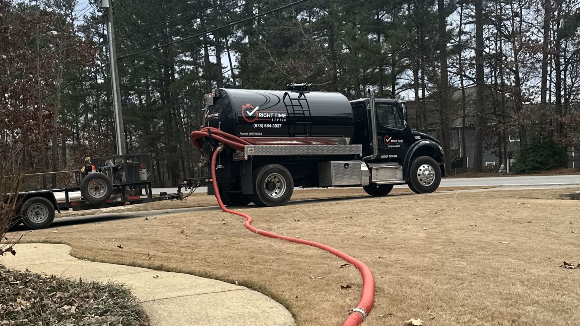 A black truck with a red hose attached to it is parked in a driveway.