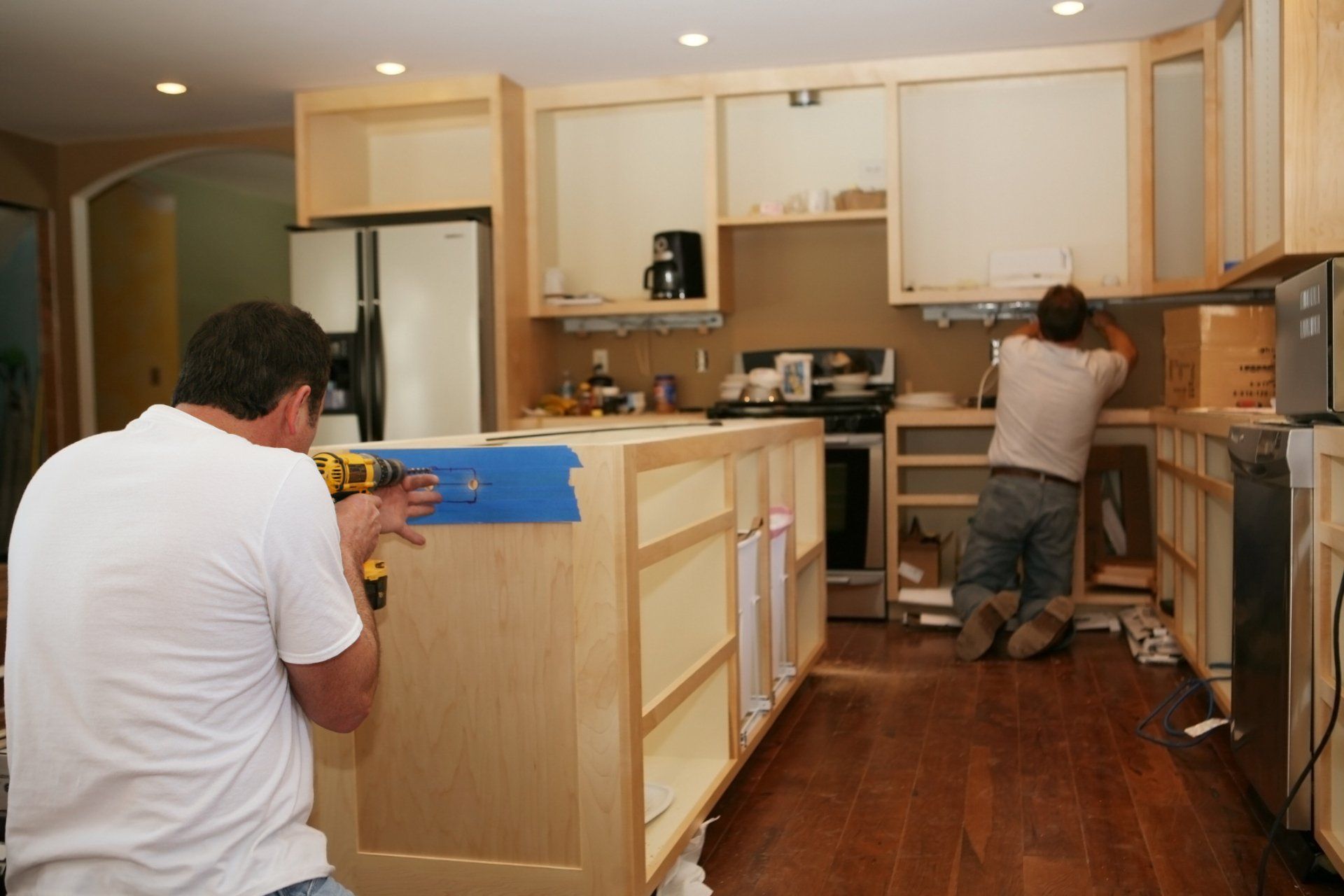 Two electricians installing electrical fixtures in a kitchen