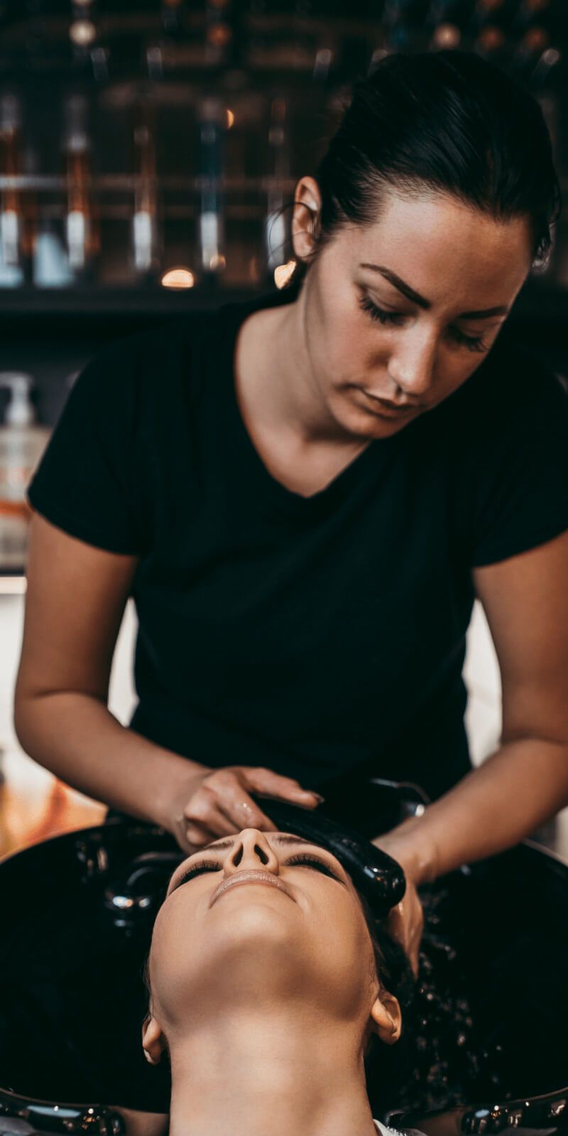 A woman is washing another woman's hair in a sink at a salon.