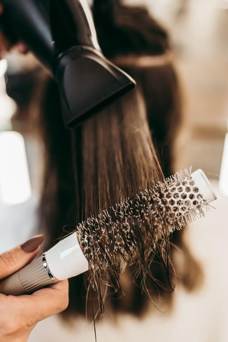 A woman is getting her hair blow dried with a blow dryer and brush.