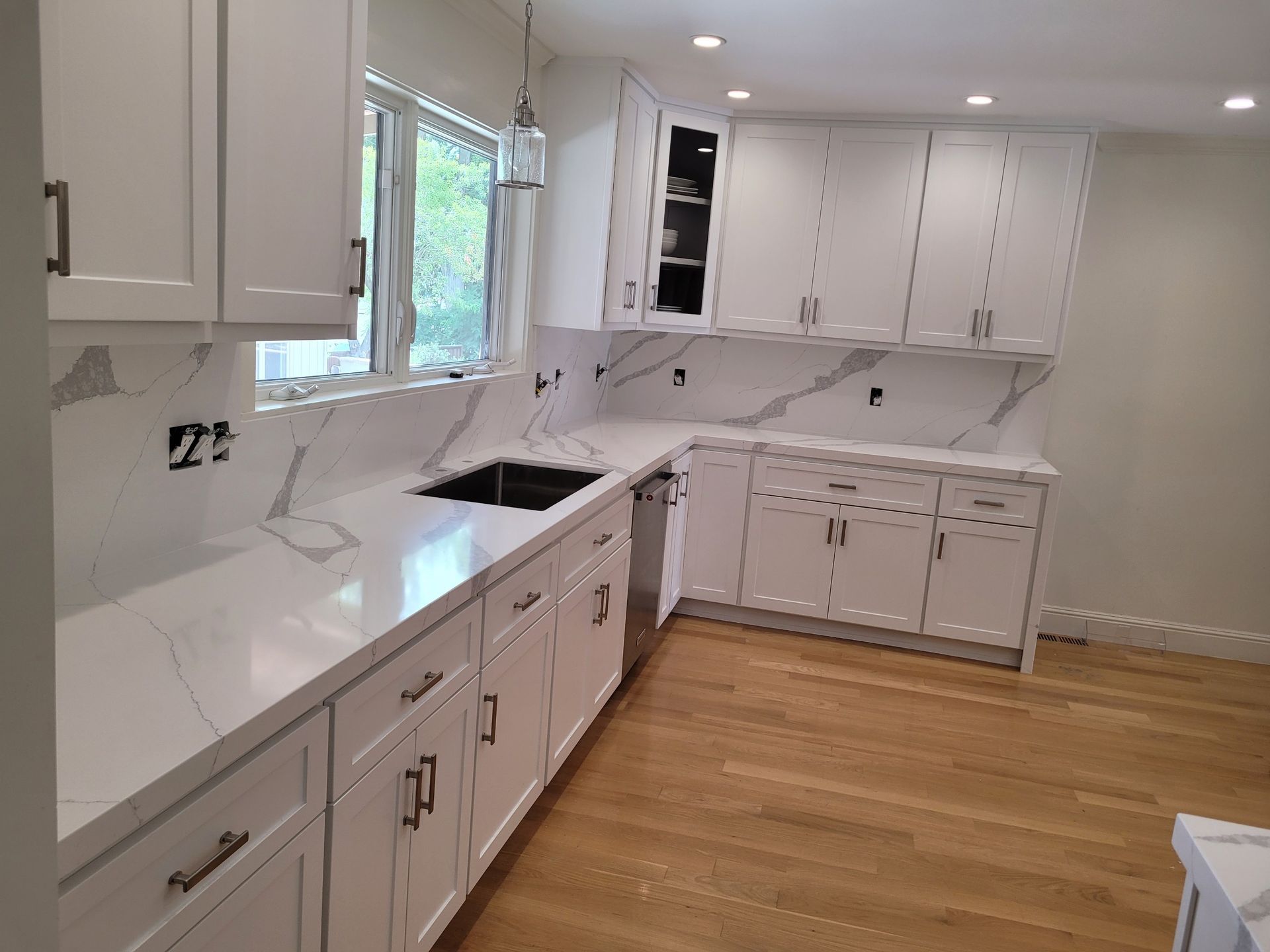 A kitchen with white cabinets , white counter tops , a sink and a window.