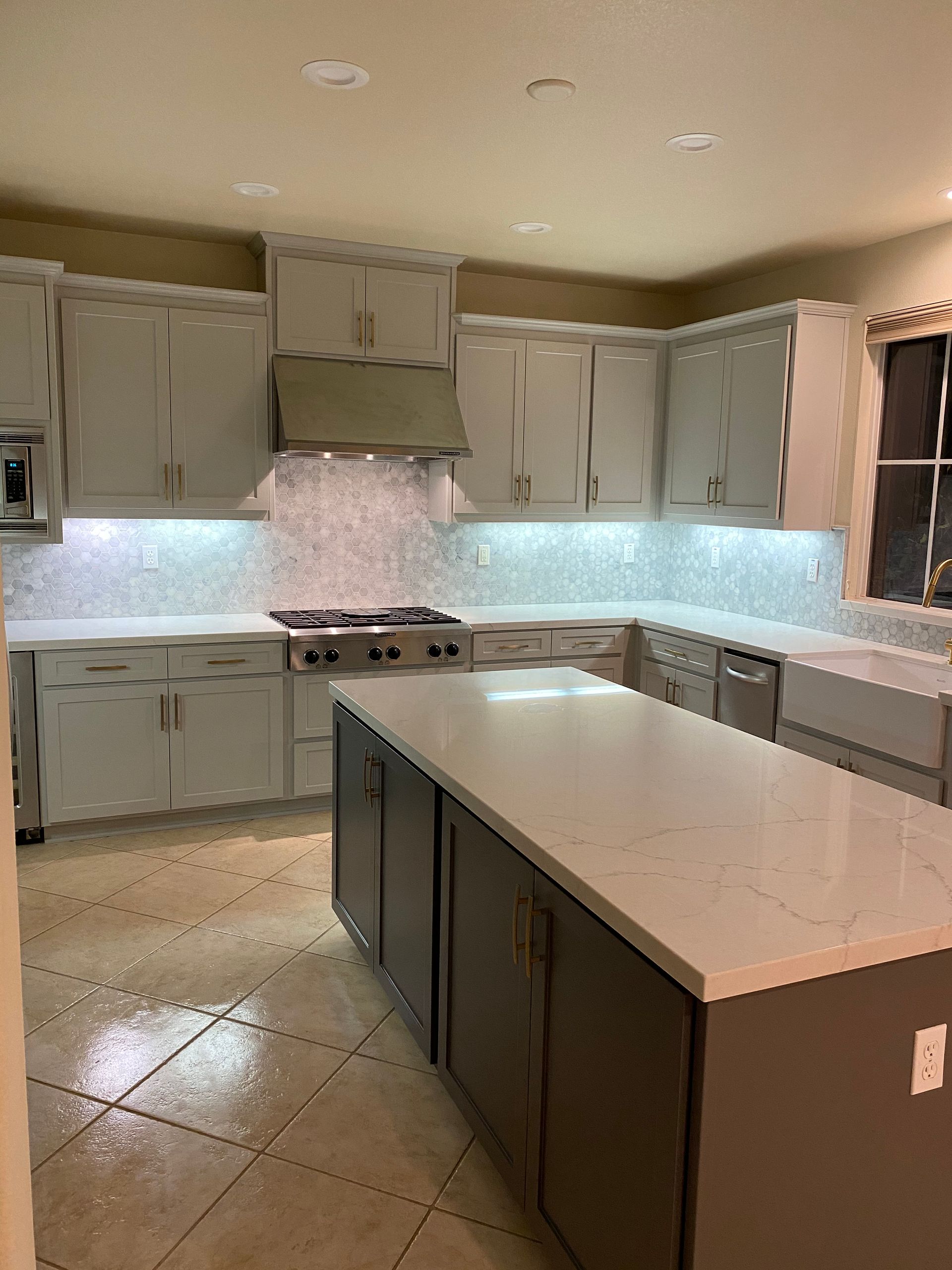 A kitchen with gray cabinets , white counter tops , and a large island.