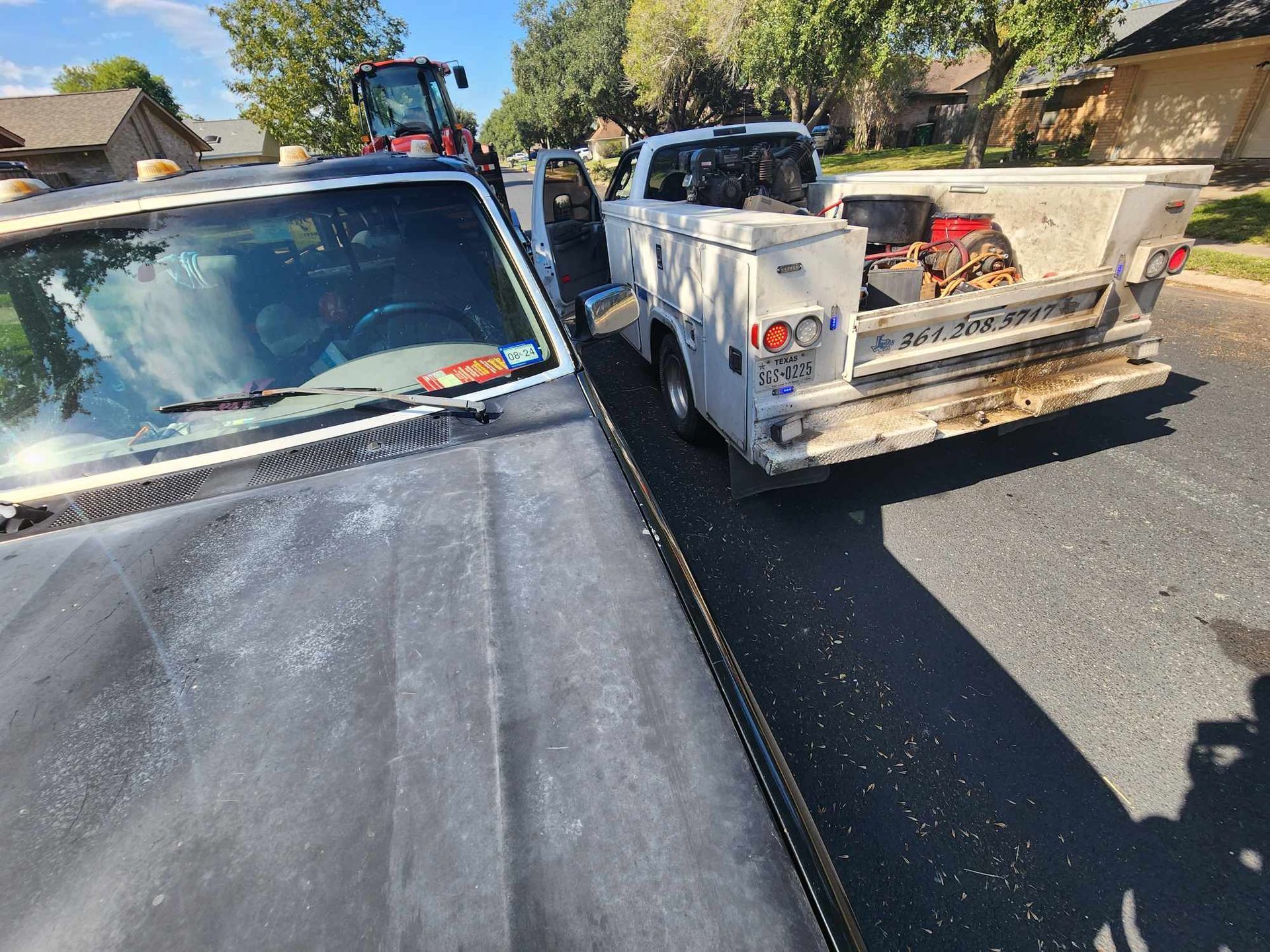 Truck parked next to a utility truck on a residential street. Tractor in the background.