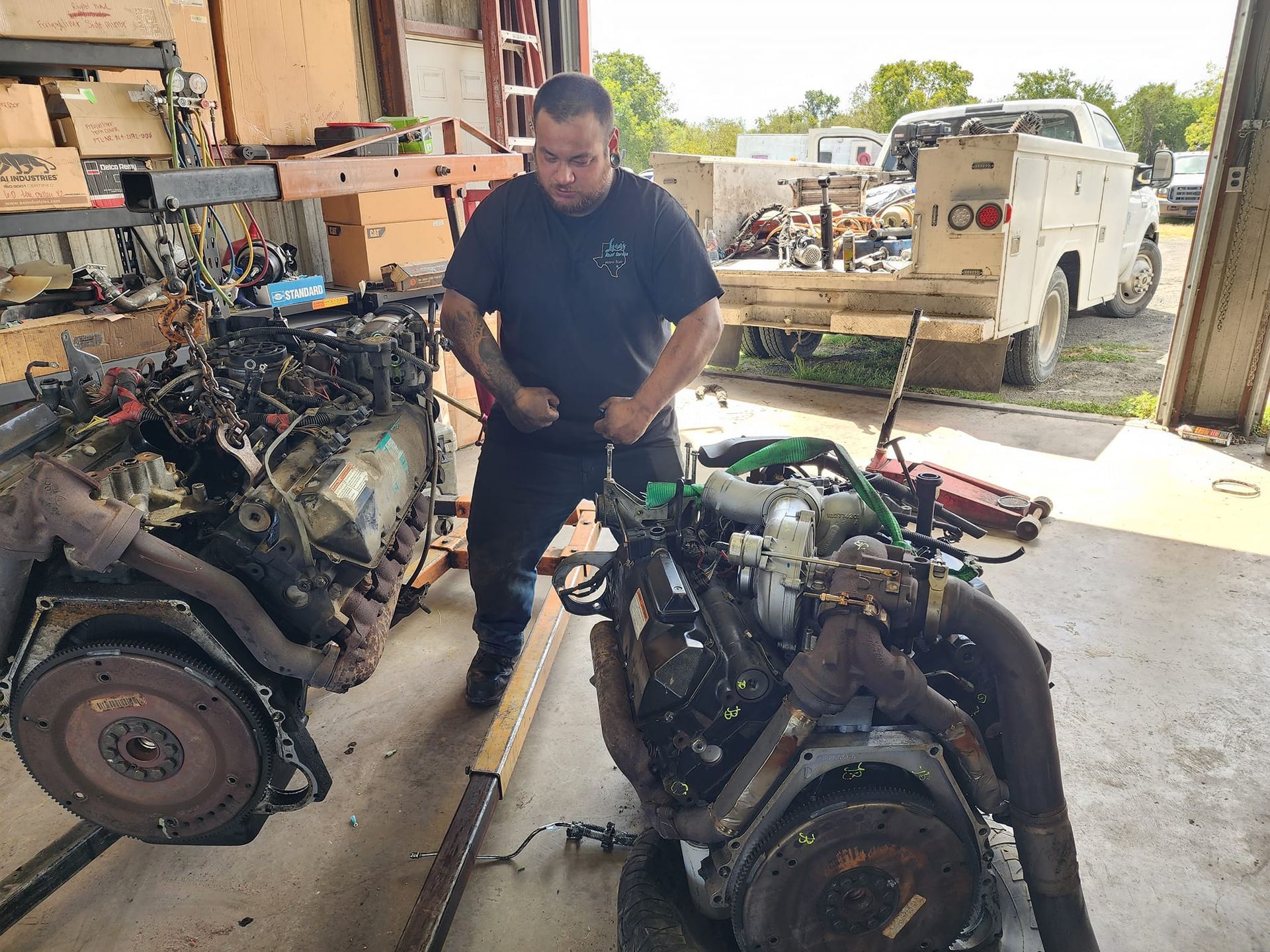 Mechanic flexes near two vehicle engines in a shop, possibly after a repair.