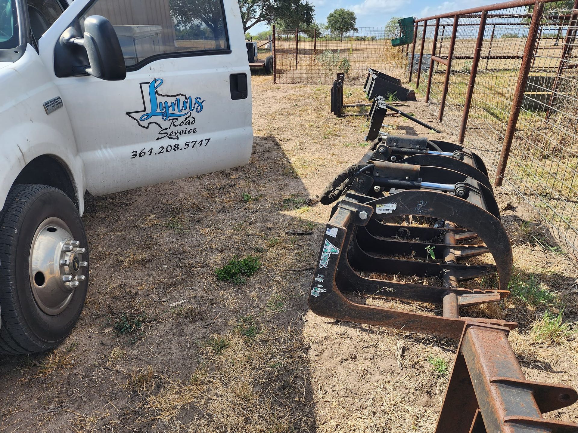 White truck parked near black grapple lying on grass.