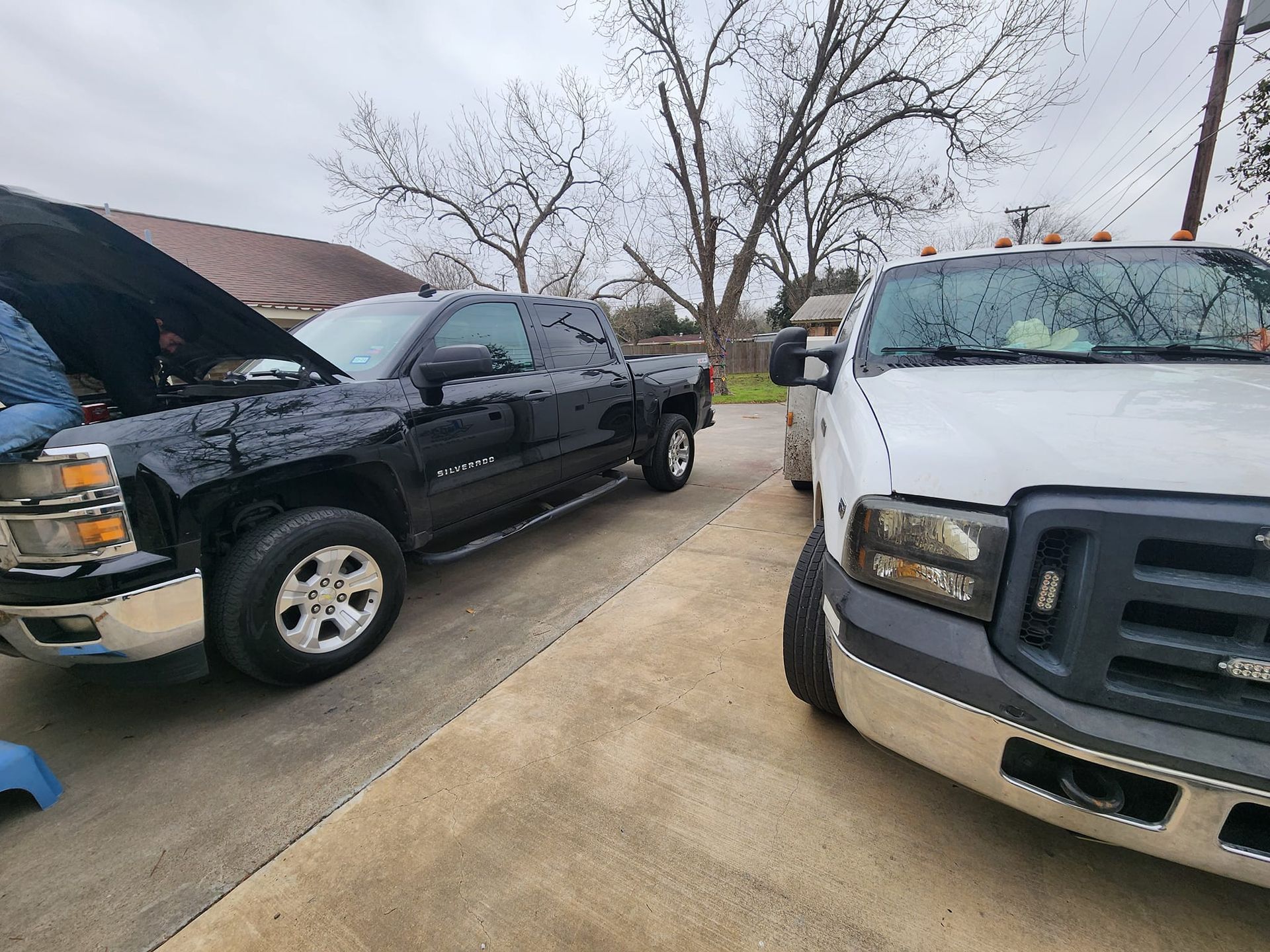 Two pickup trucks parked outside on a cloudy day. One is black, the other white.