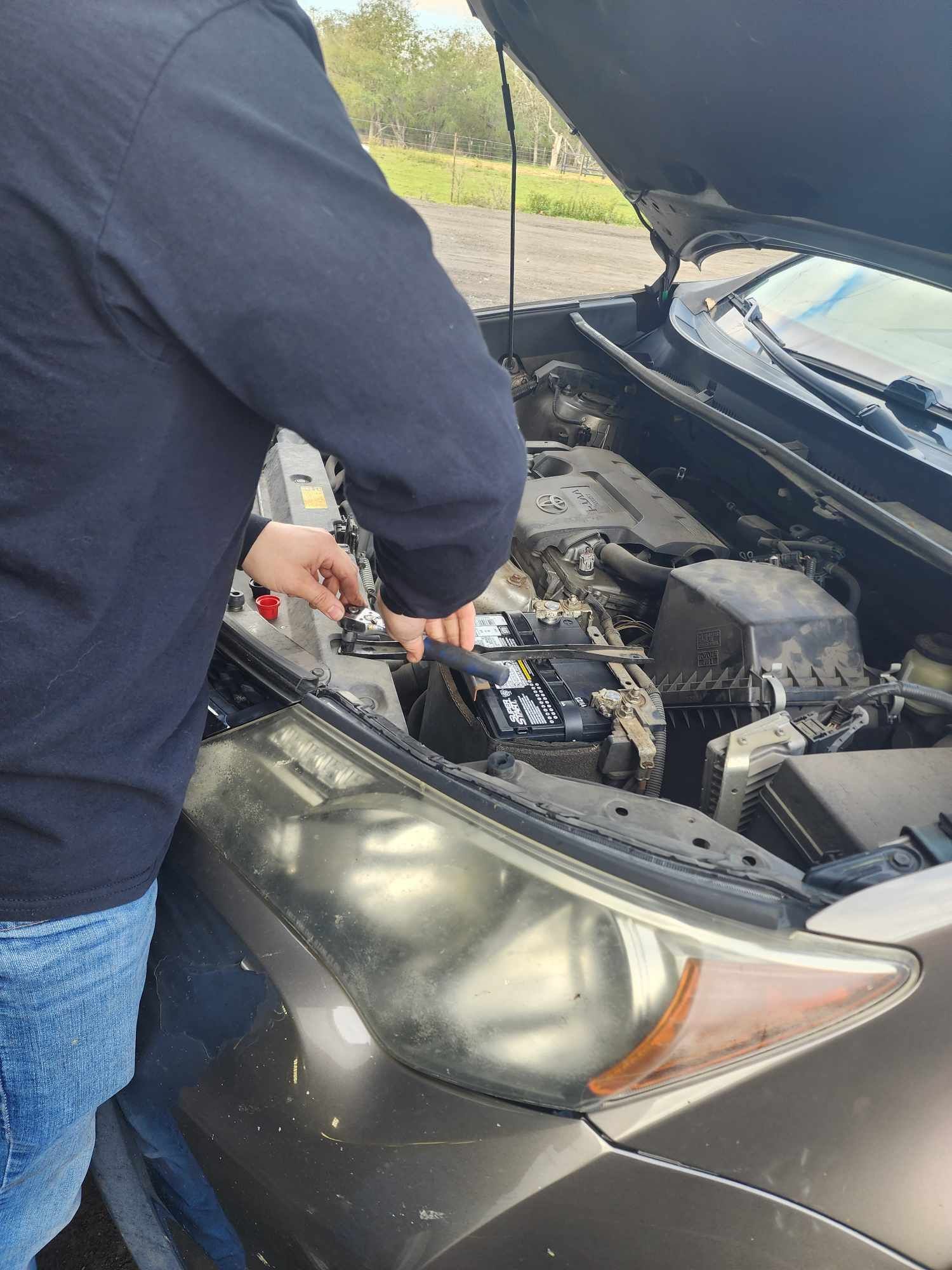 Person working on a car engine with the hood open outdoors.