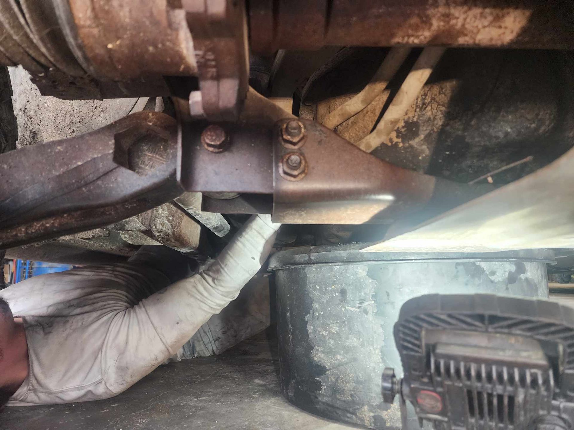 Mechanic working on a vehicle's undercarriage with a wrench, a drain pan, and work light.