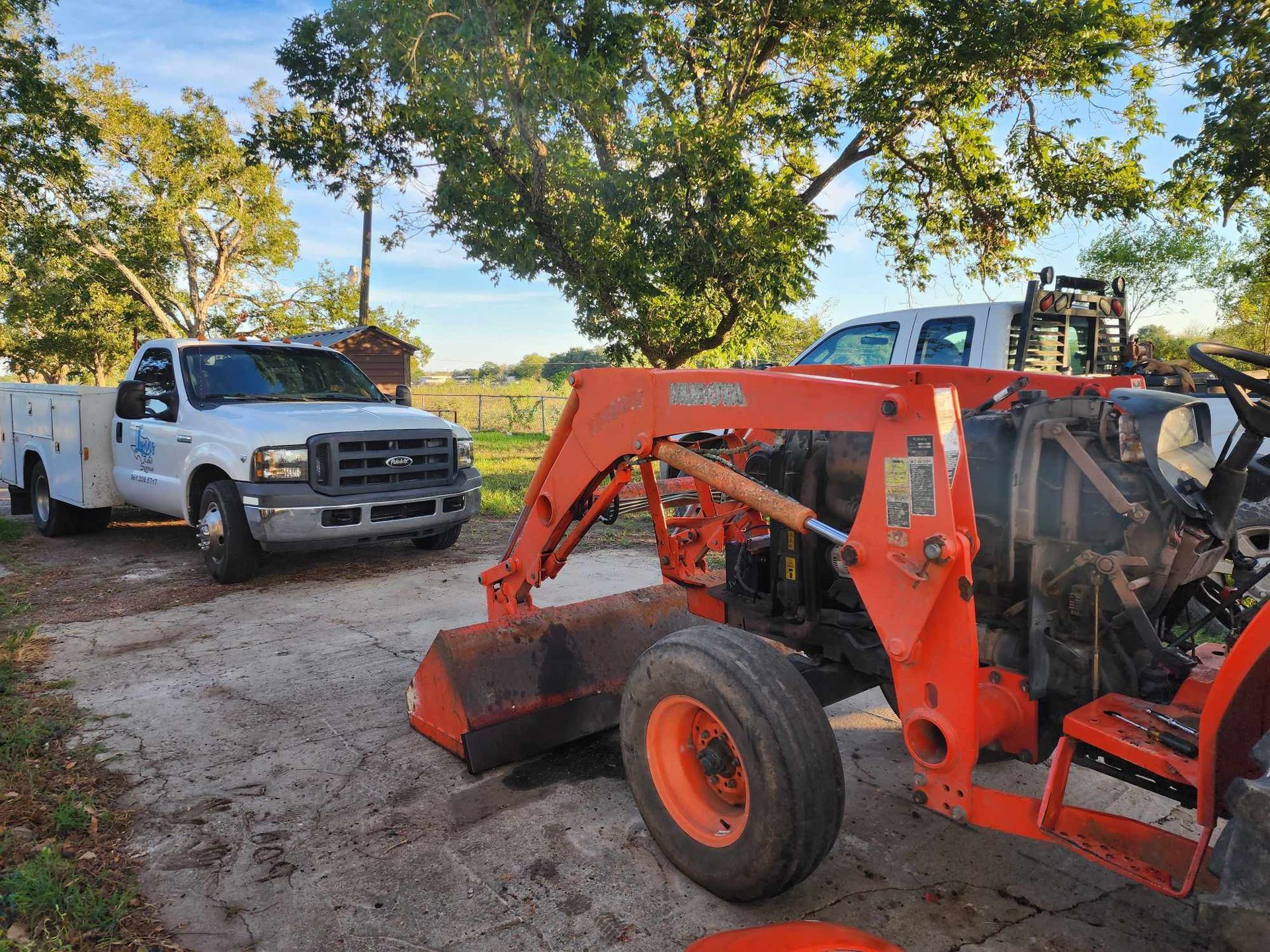 White truck and orange tractor parked outside in a daytime setting.