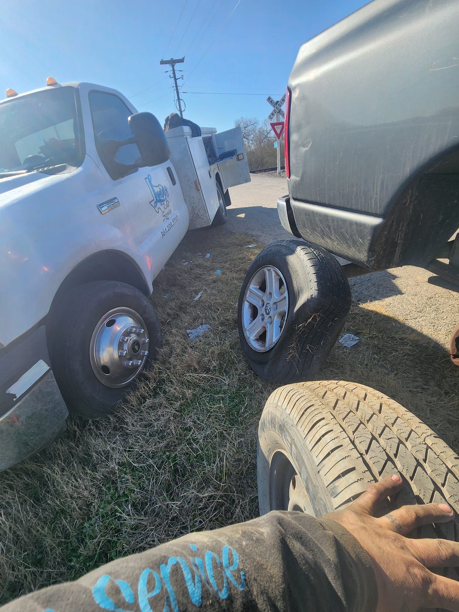 Tow truck assisting a grey truck with a flat tire on a grassy area.
