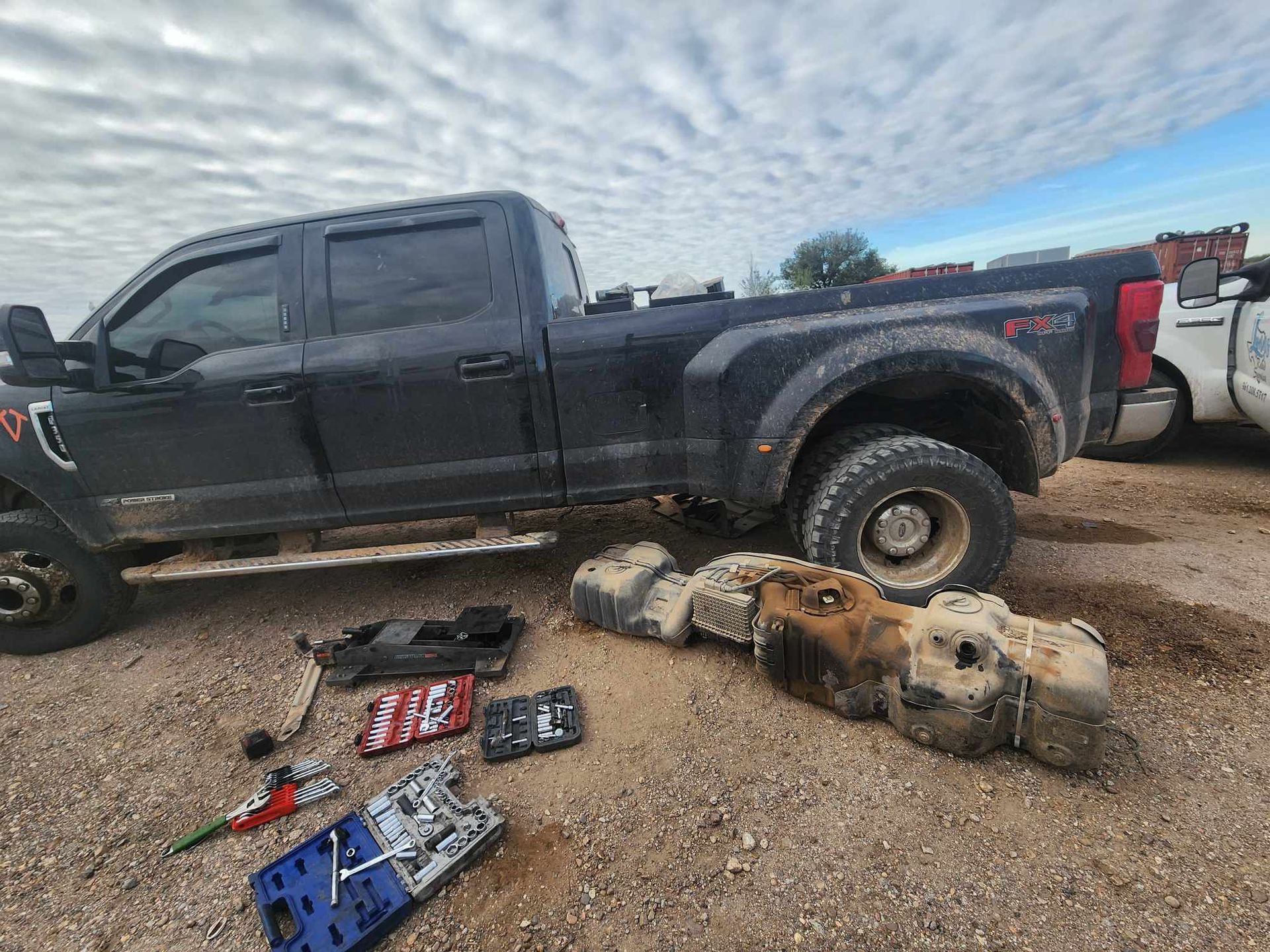 Black pickup truck with a detached fuel tank and other debris on a dirt surface.