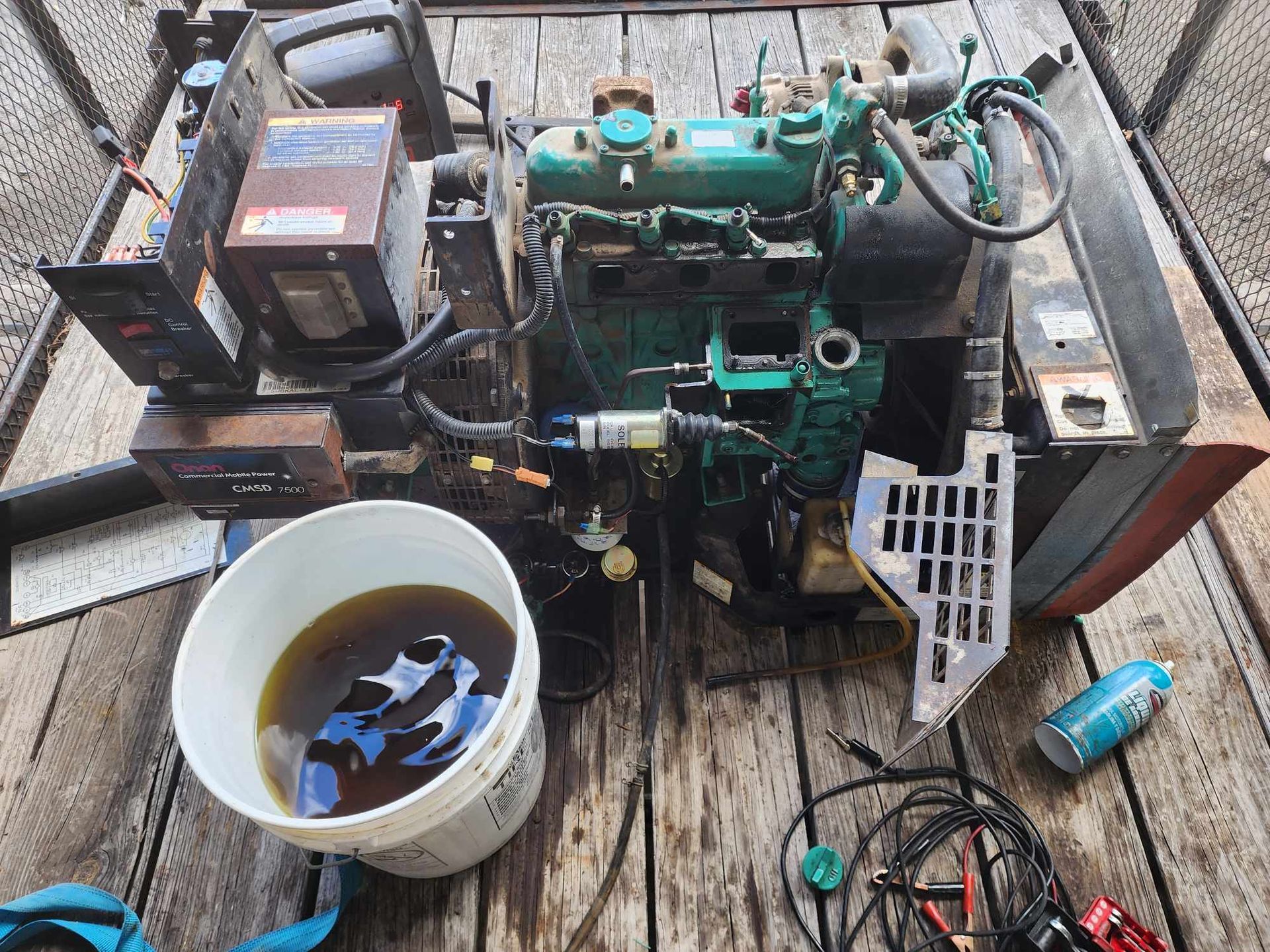 Diesel engine on wooden surface with bucket of oil, tools, and electrical components.