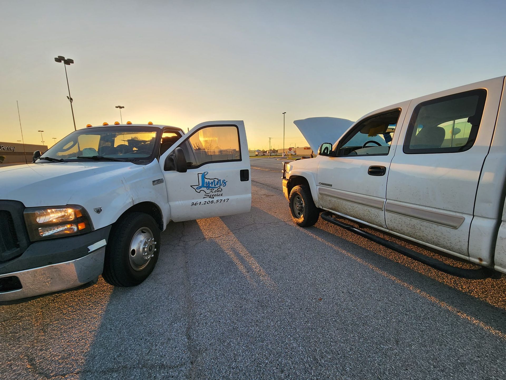 Two white work trucks parked outdoors at sunset. One door open, sun in frame.
