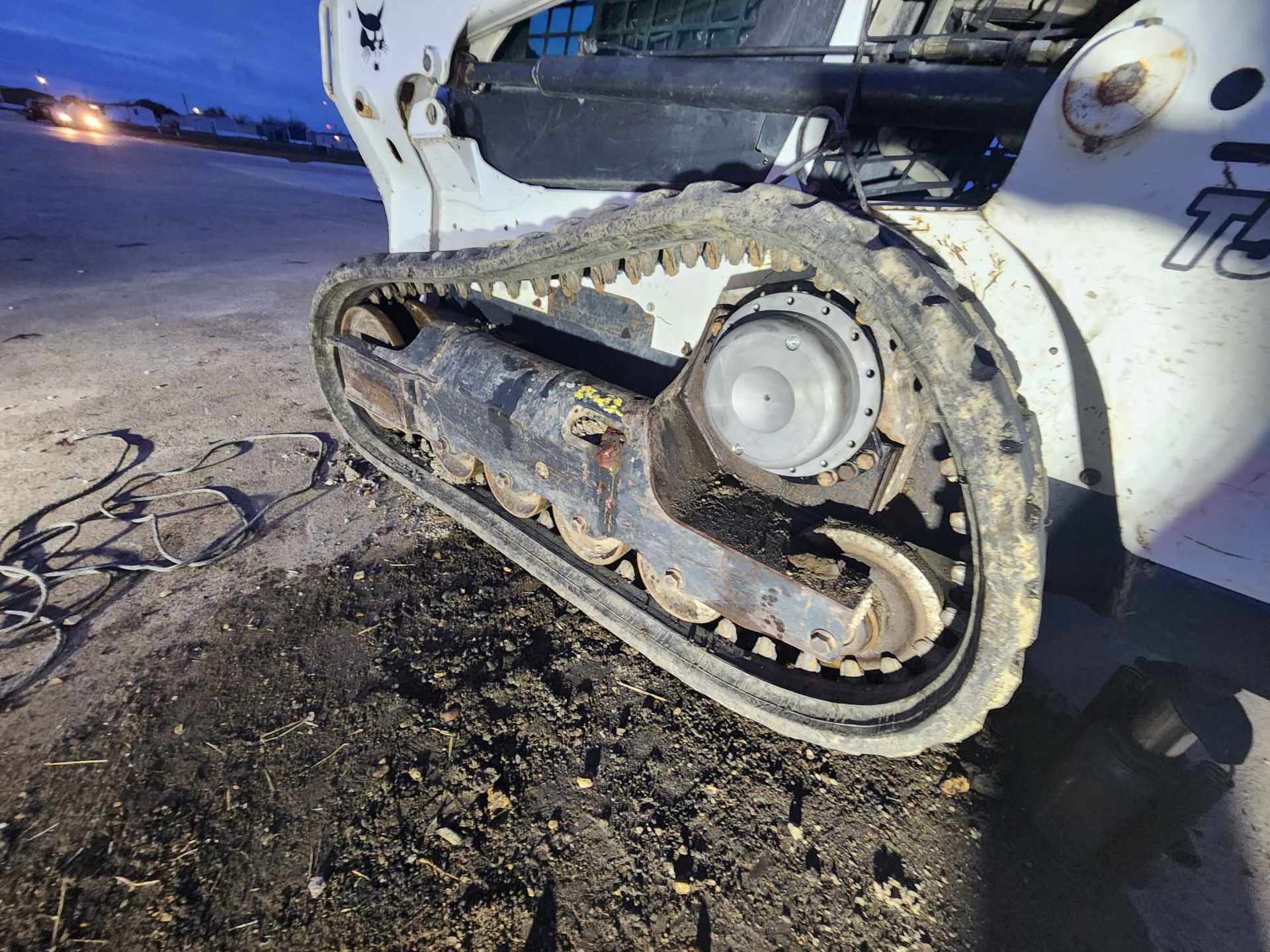A close-up view of a Bobcat track loader, covered in dirt, sitting on a muddy surface.