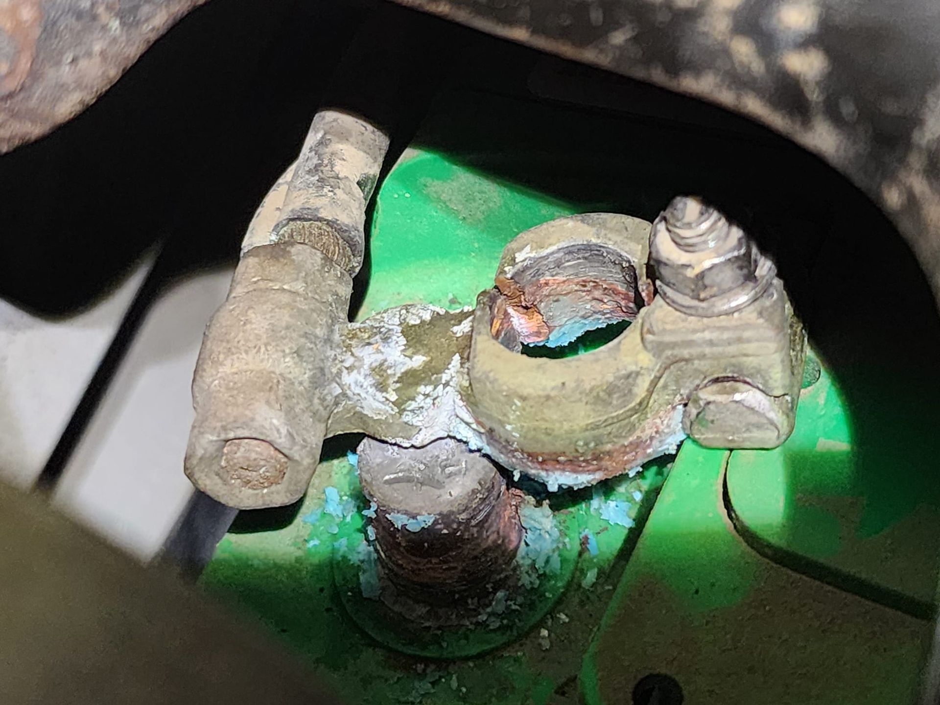 Corroded car battery terminal with white and blue residue on green battery casing.