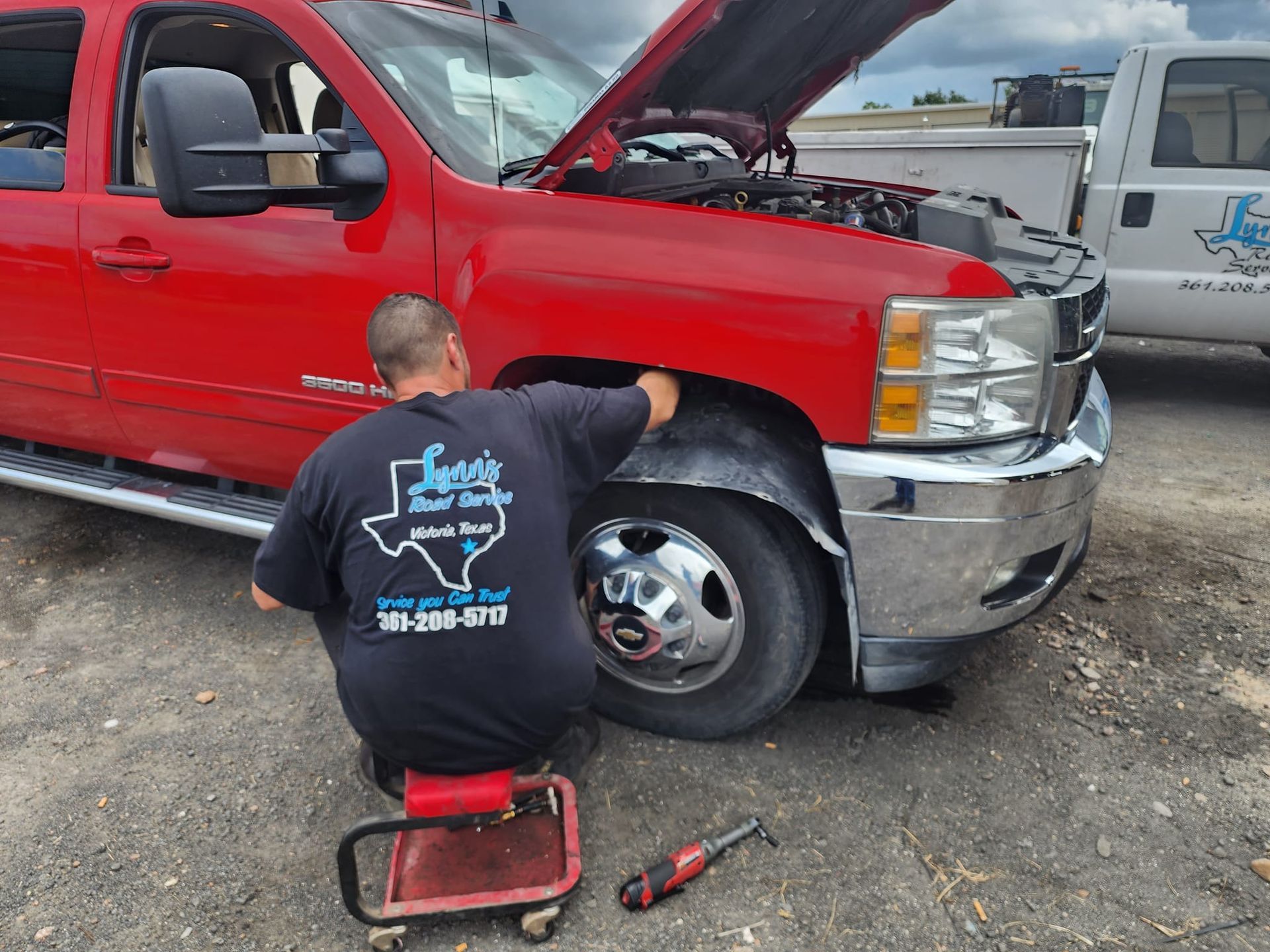 Man working on a red truck's wheel well, wearing a black shirt with Texas logo, outdoors.