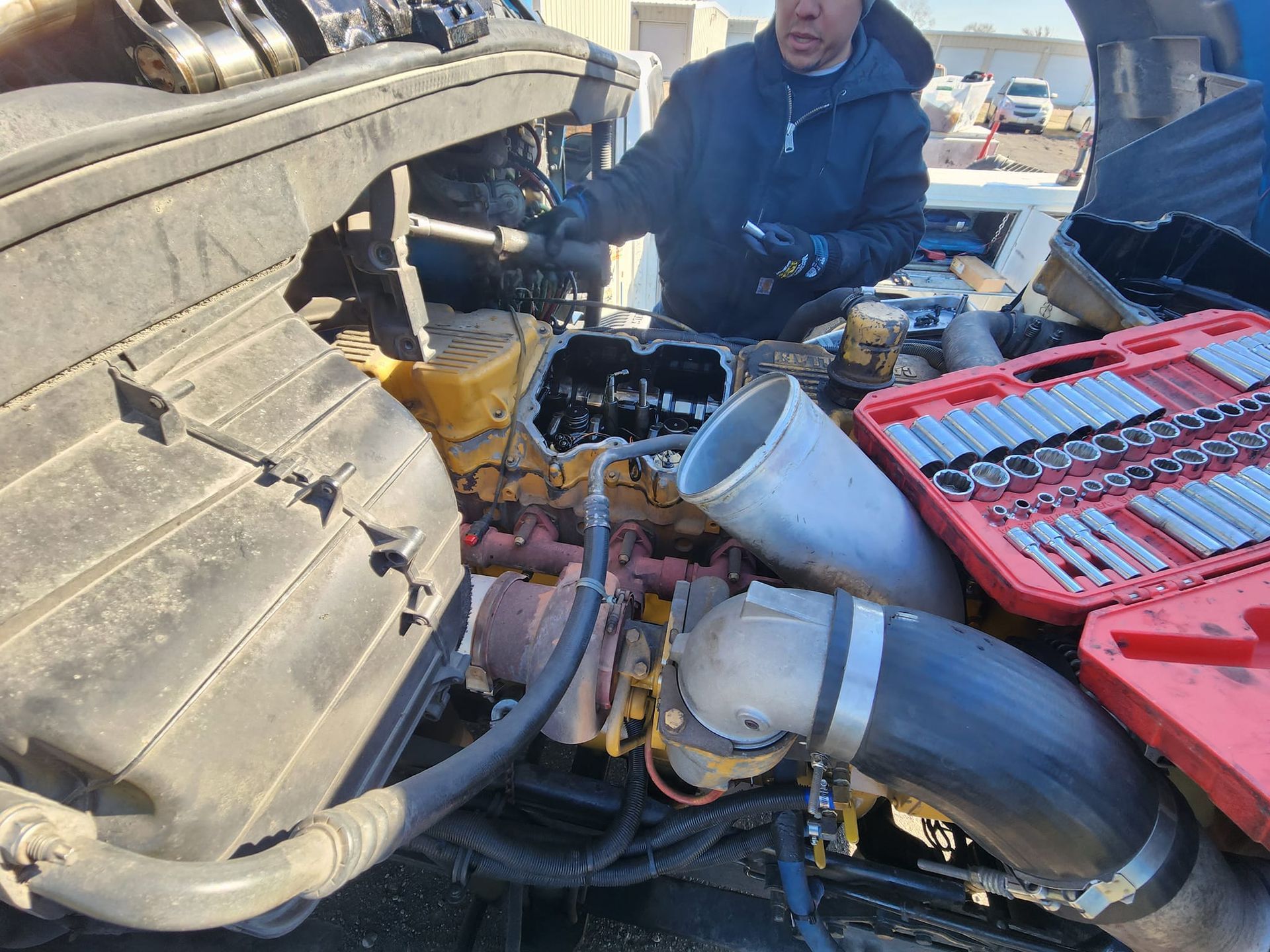 Mechanic working on a truck engine, tools laid out; outdoors.