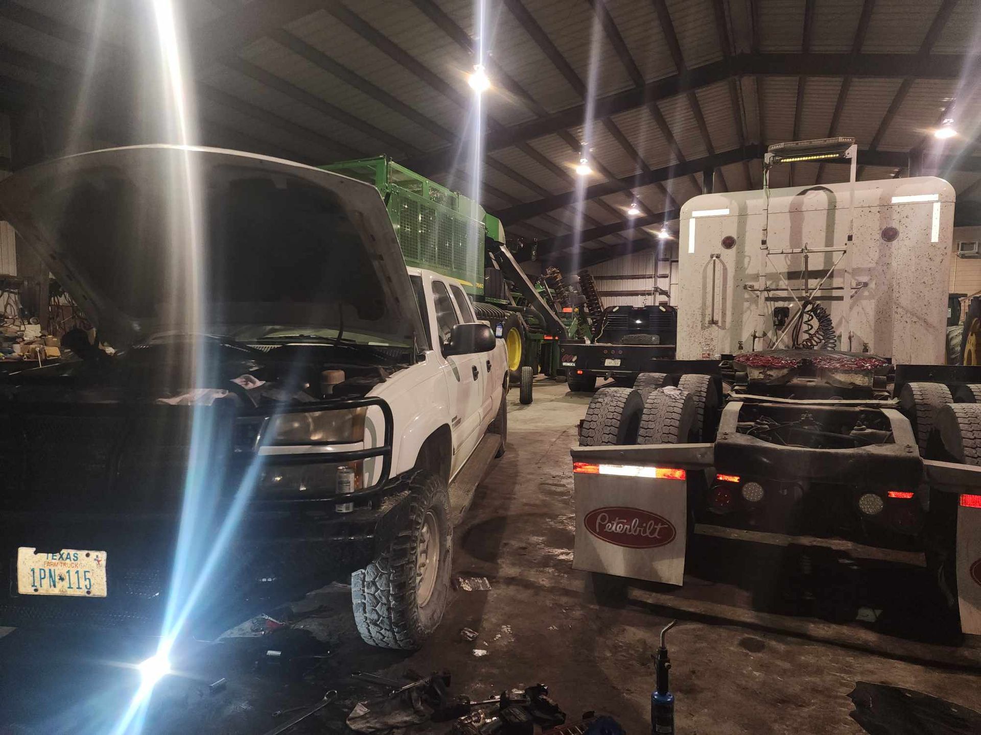 White truck with hood open, next to a semi truck in a shop, illuminated by lights.