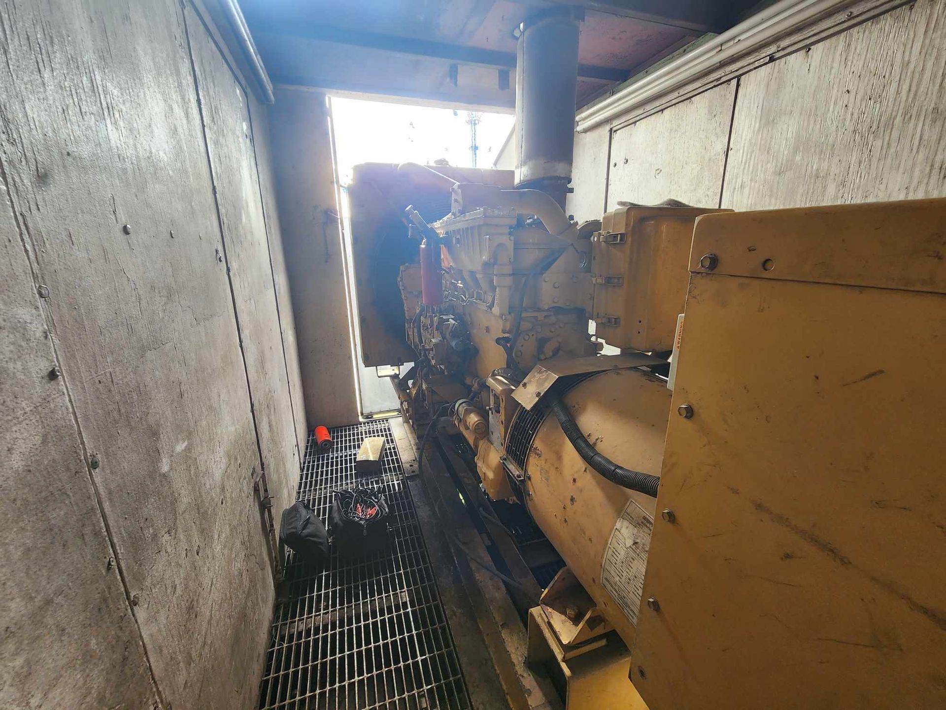 Yellow generator inside a concrete enclosure with a metal grate floor.