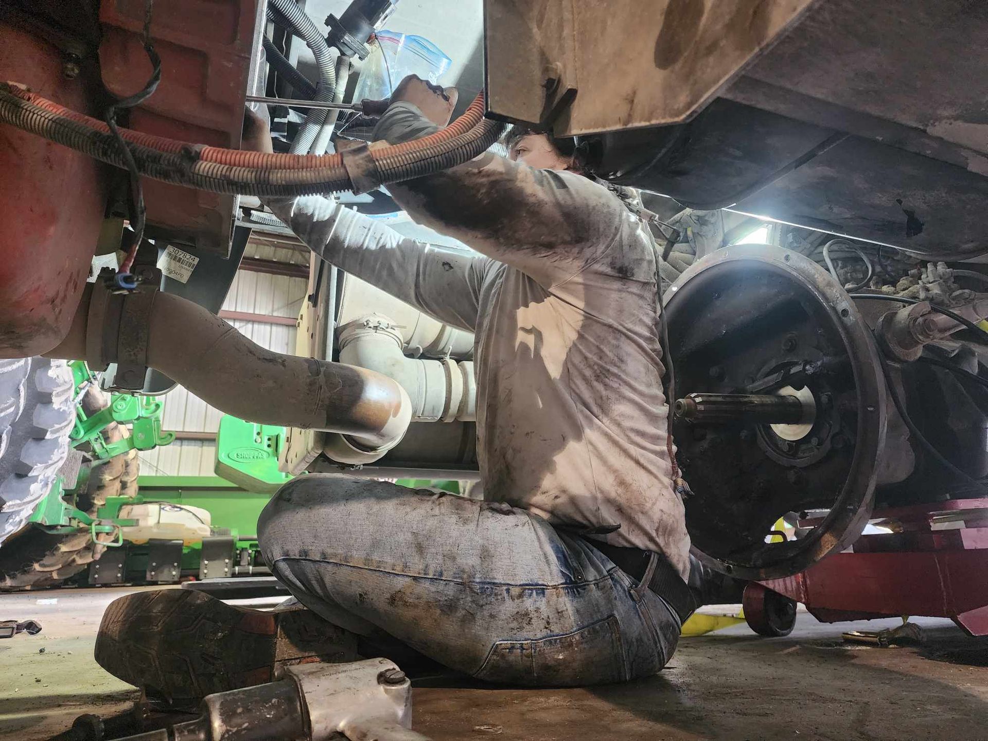 Mechanic working on a vehicle, covered in dirt, inside a repair shop.