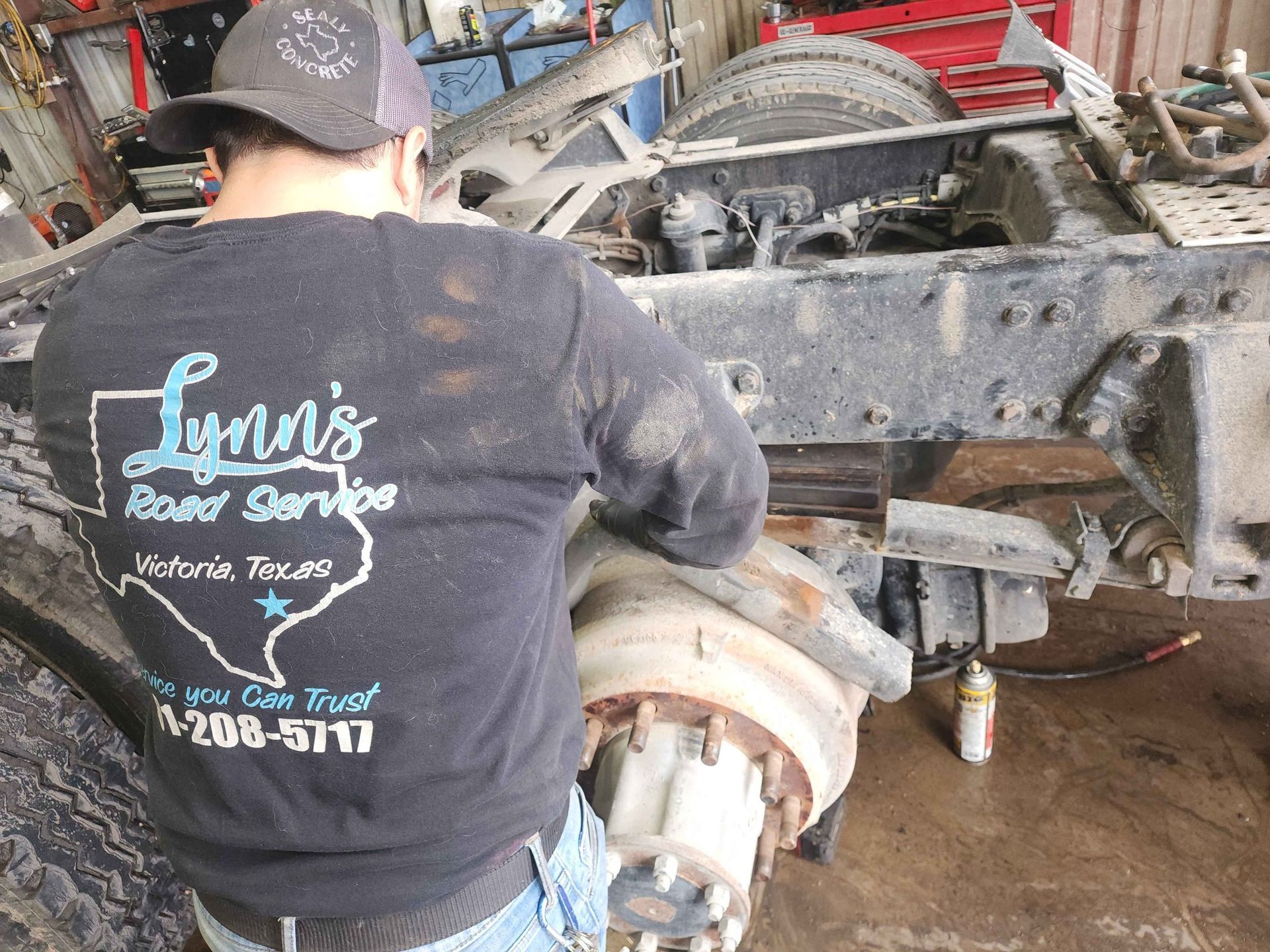 Mechanic working on a truck wheel in a shop. They wear a shirt for Lynn's Road Service in Victoria, TX.