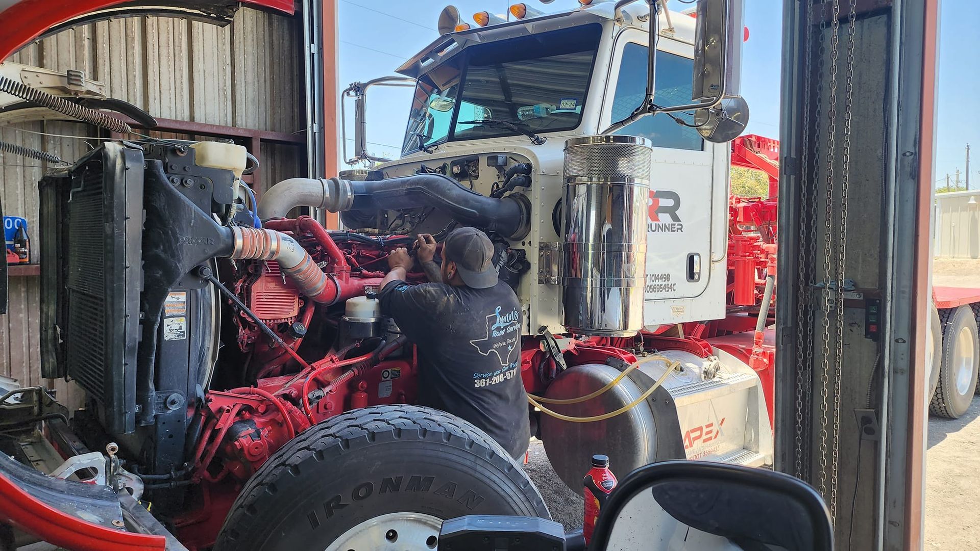 Mechanic working on a red and white semi-truck engine in a garage.