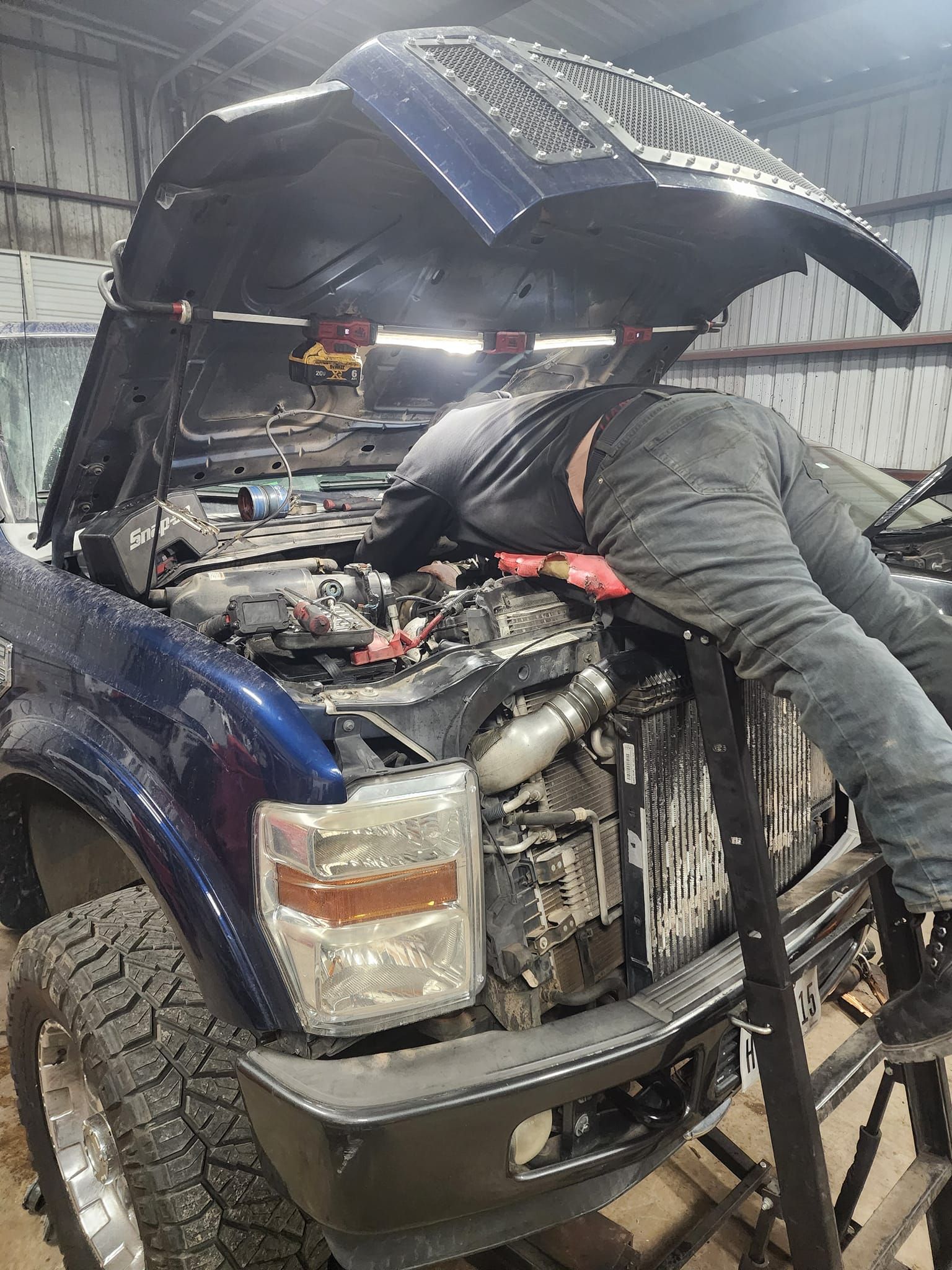 A person working on a blue truck engine with the hood open in a garage.
