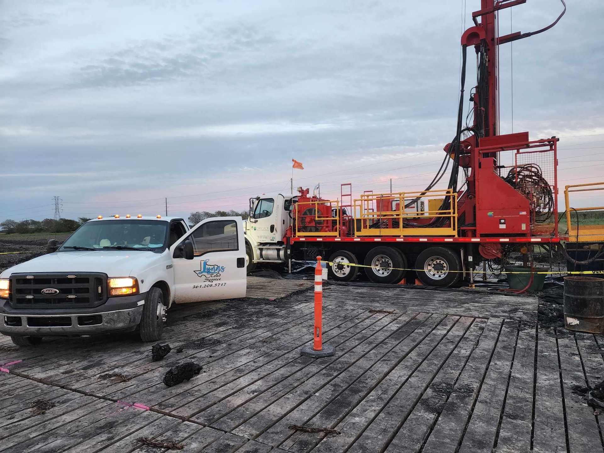 A white truck and drilling rig on a wooden platform. The sky is overcast.