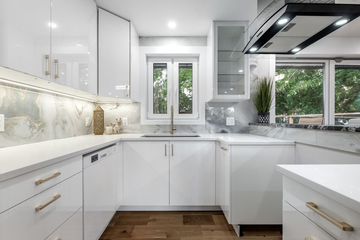 Bright modern white kitchen with marble counters, gold accents, and a window over the sink
