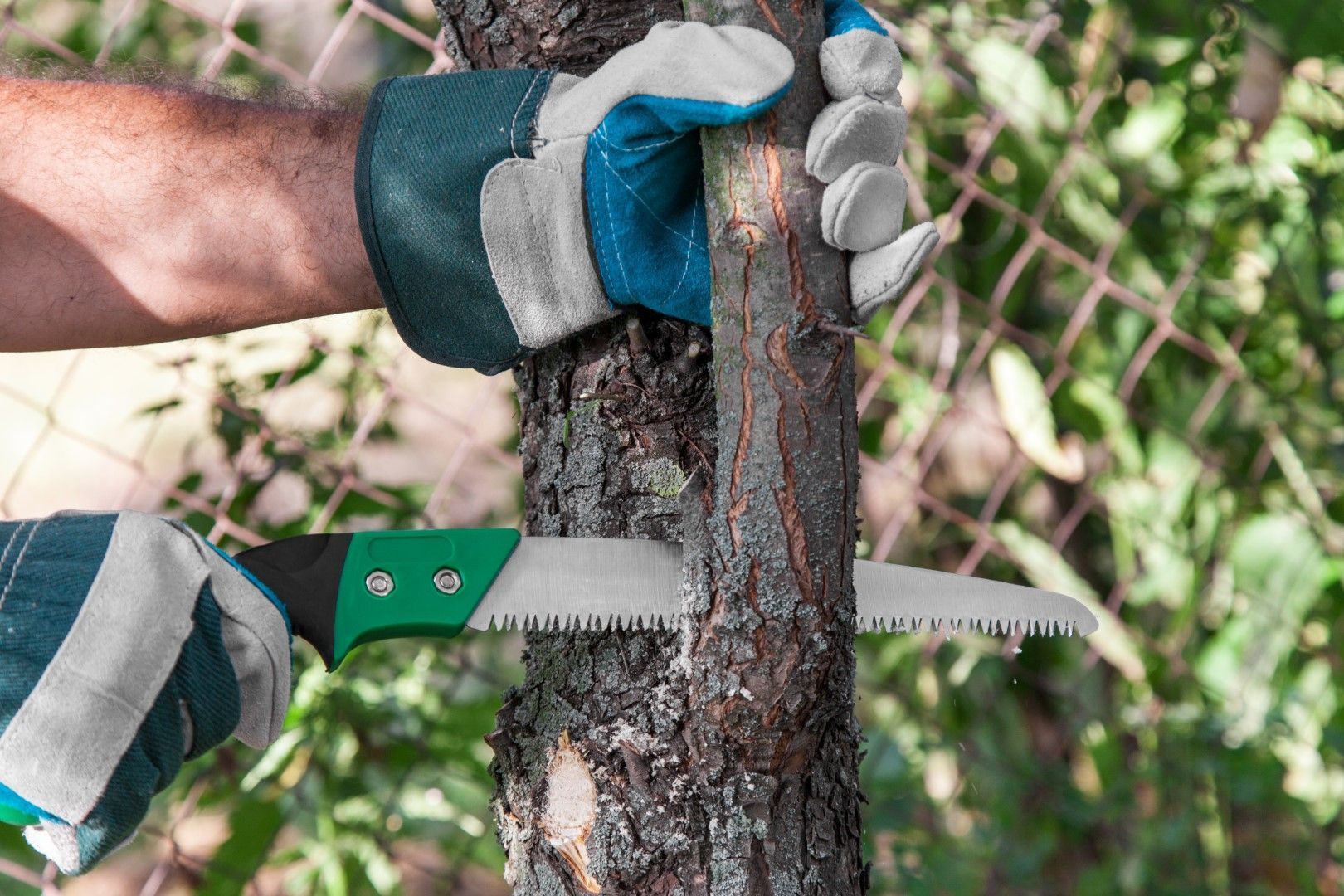 Gloved hands cutting a tree trunk with a handsaw outdoors