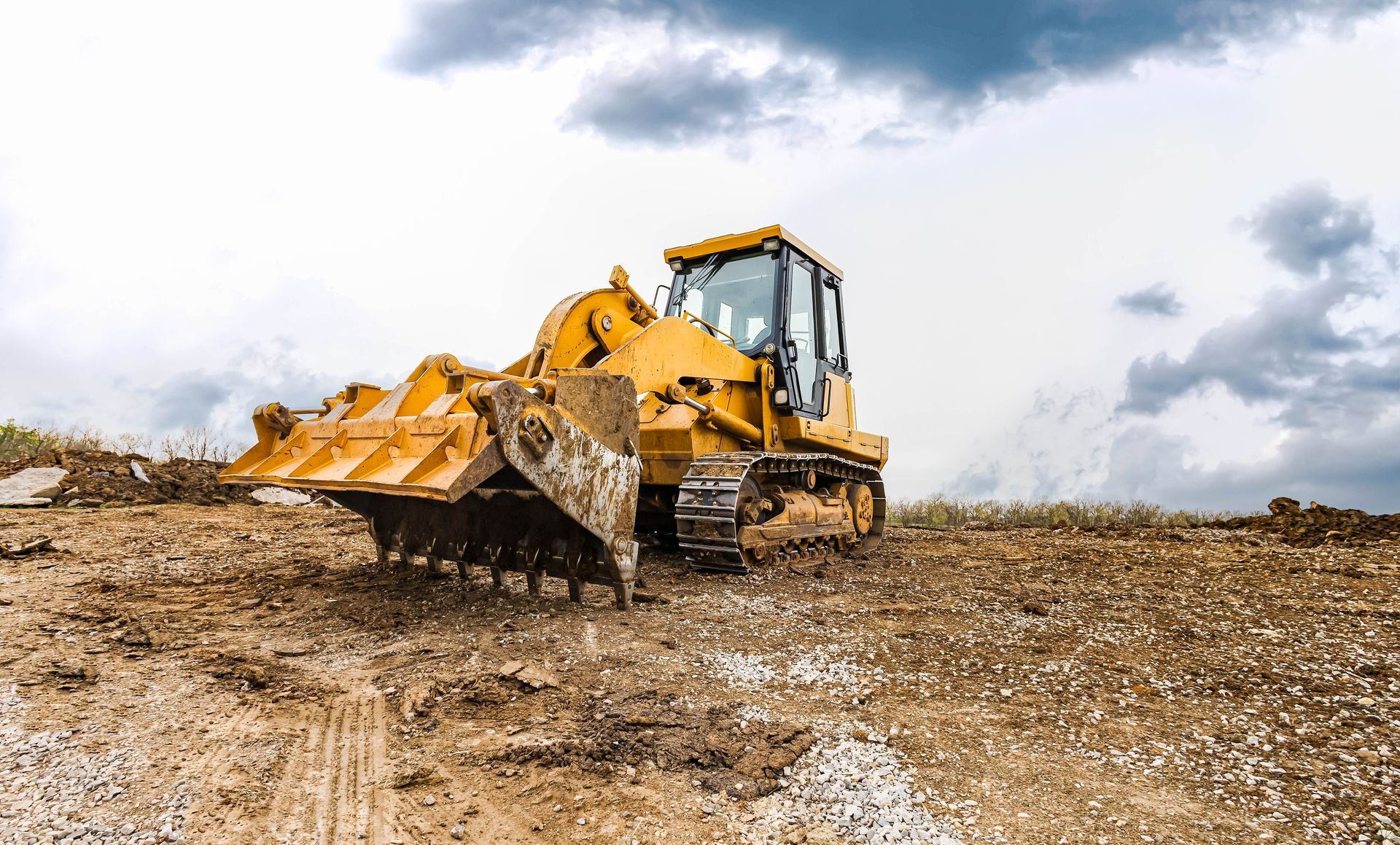 Yellow bulldozer grading a muddy dirt field under a cloudy sky
