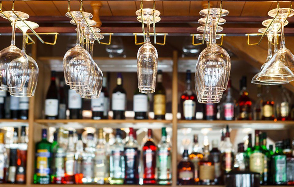 A bar with wine glasses hanging from the ceiling and bottles on the shelves.